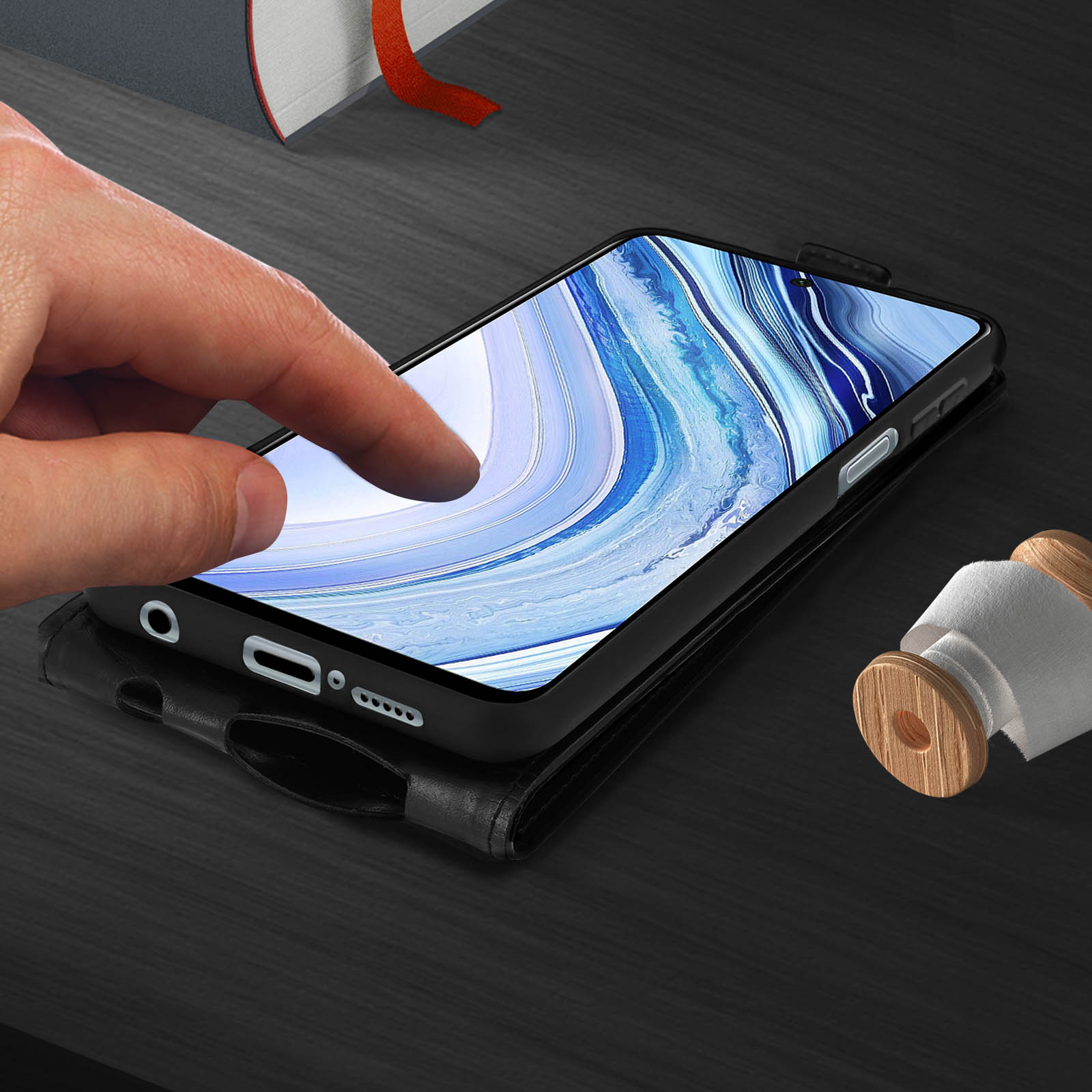 Un doigt touche l'écran d'un smartphone noir dans un étui en cuir.