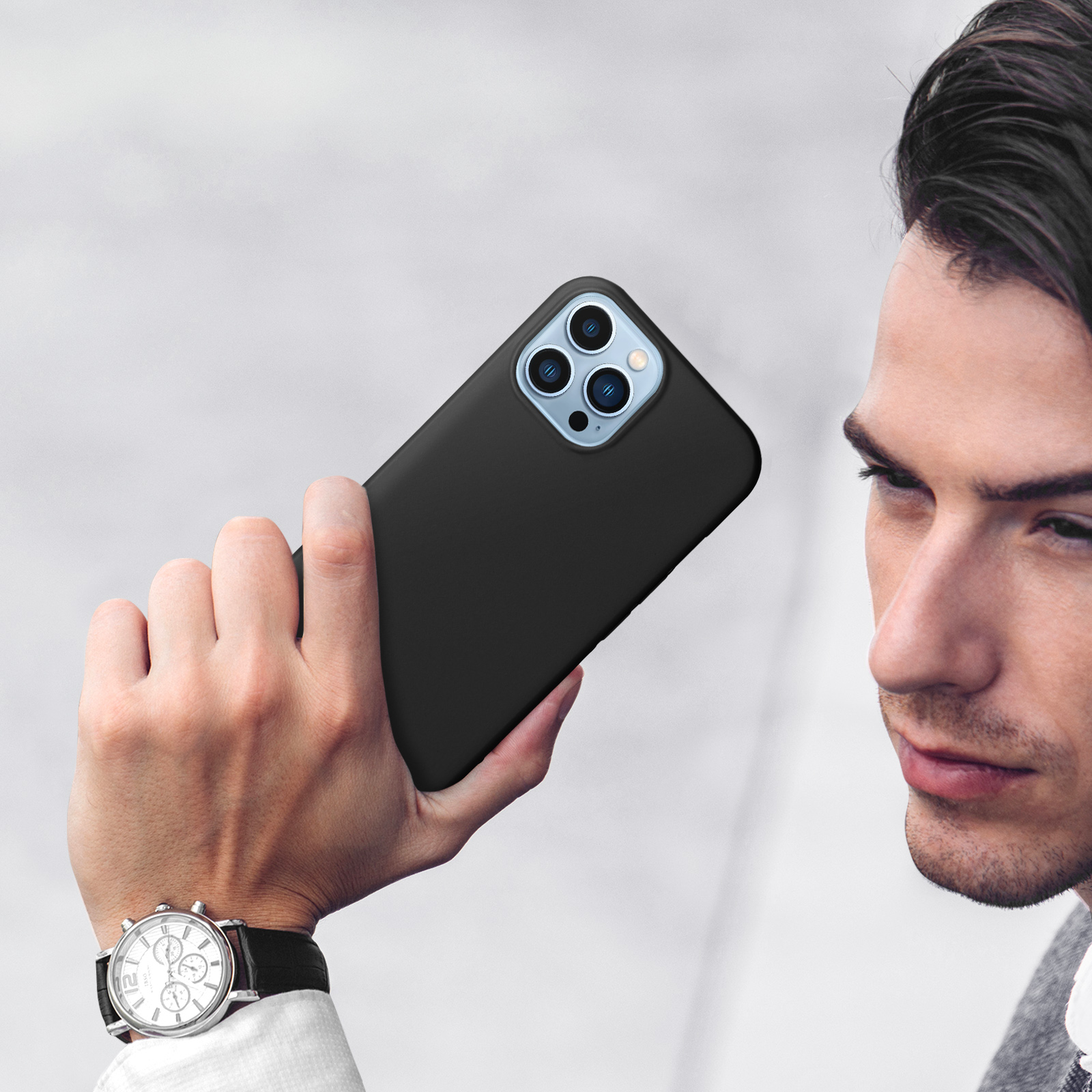 Uomo che tiene un iPhone nero con tre fotocamere, indossa un orologio.