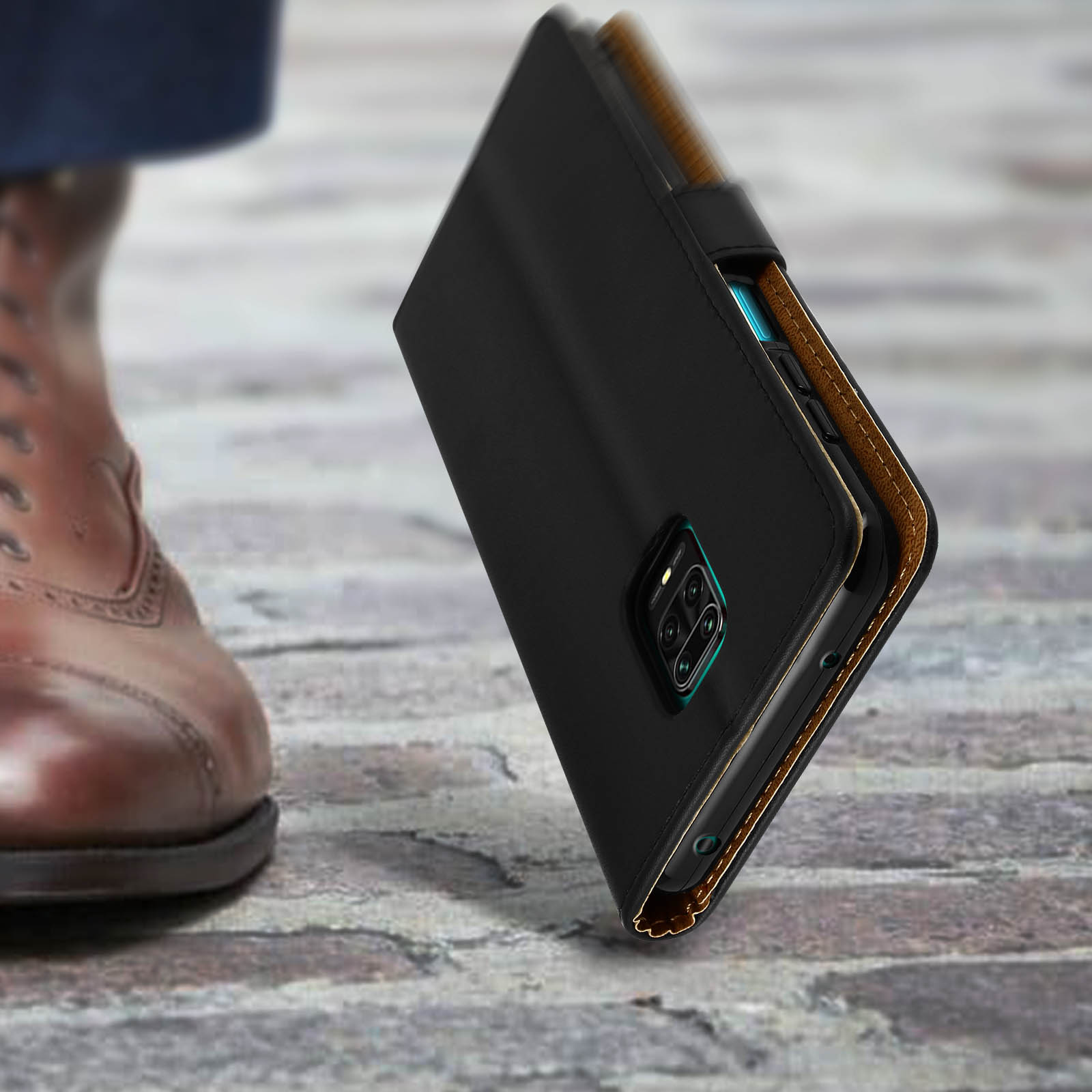 Étui portefeuille noir à bord marron sur fond de pierre, à côté d'une chaussure marron.