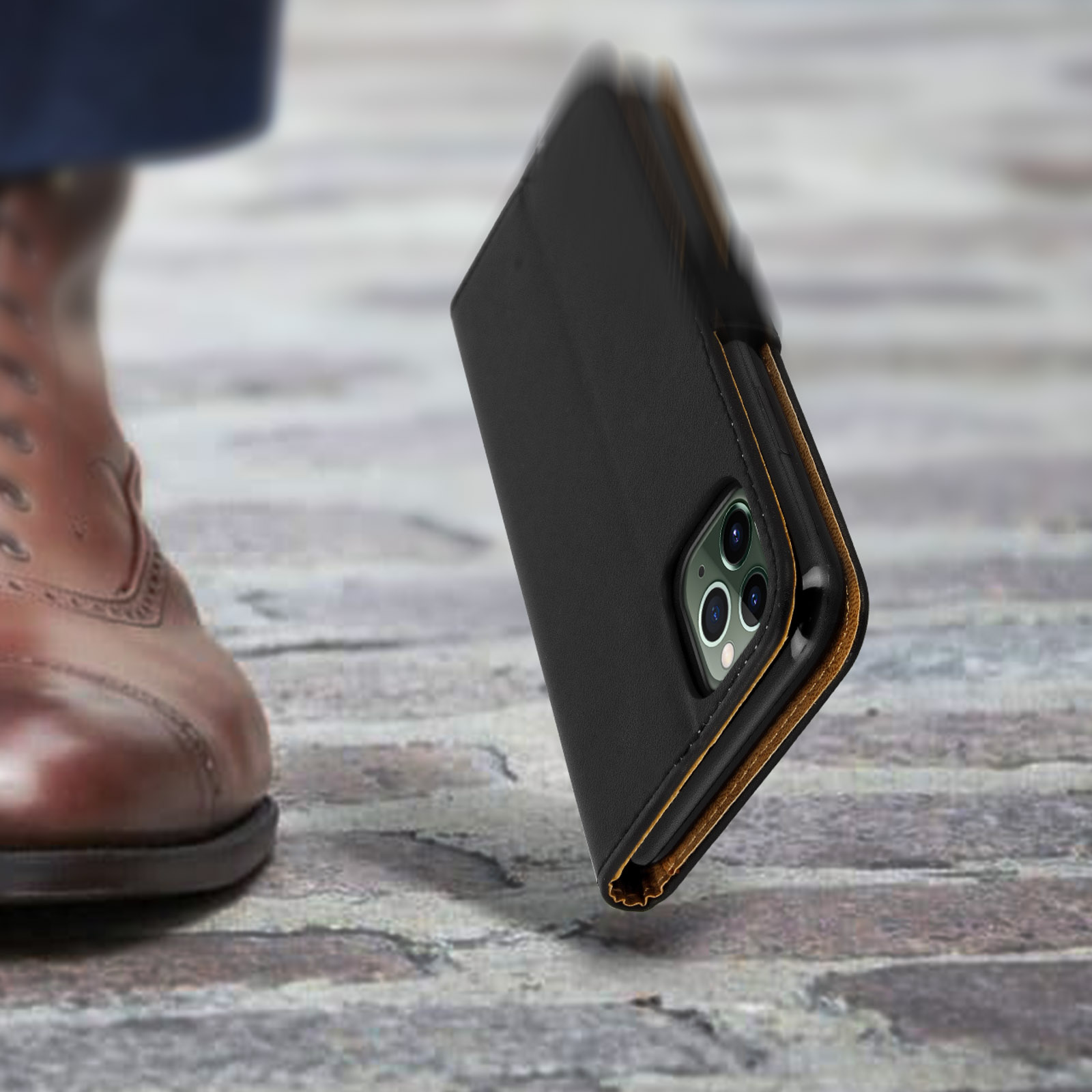 Une coque de téléphone noire avec trois caméras tombe sur un sol en pierre.