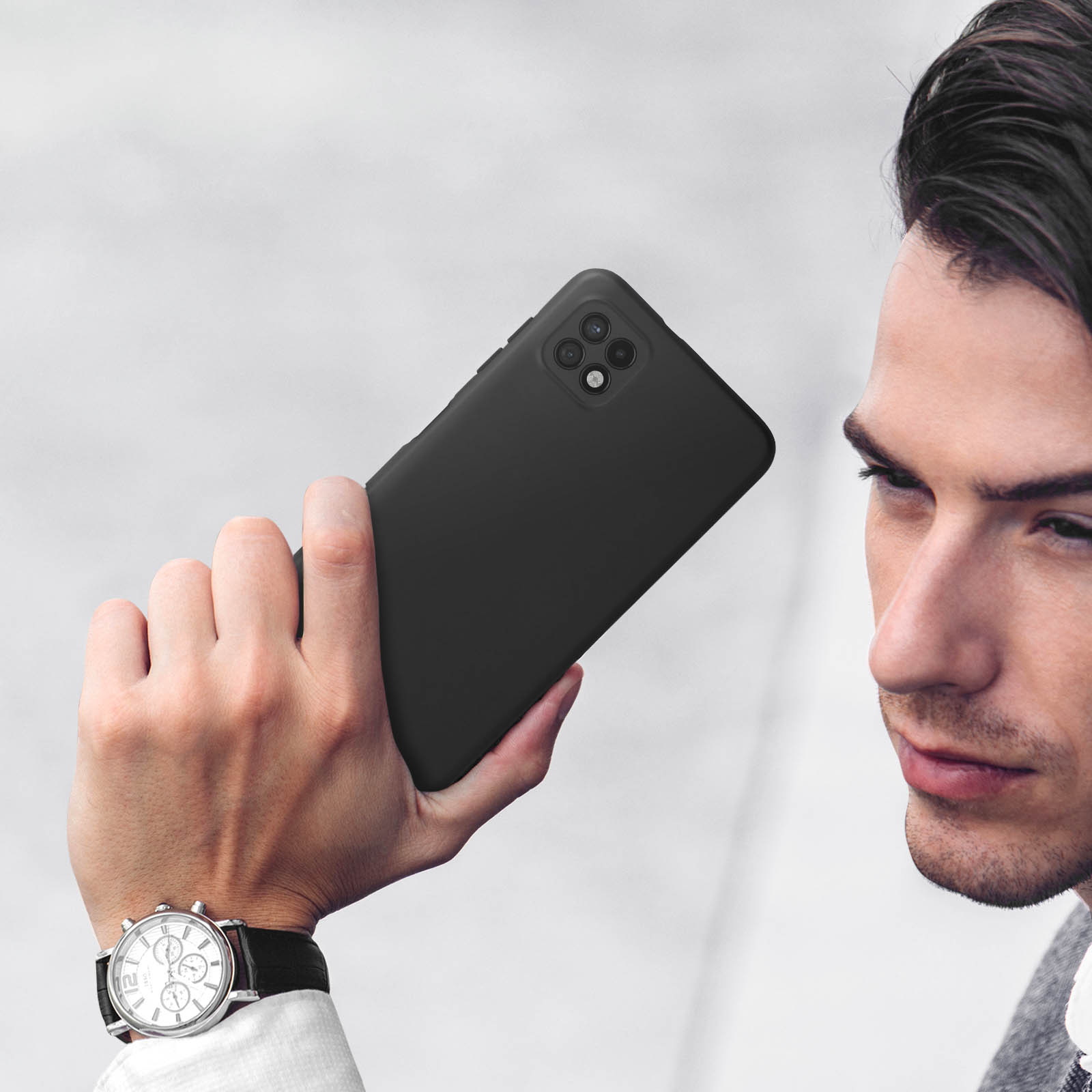 Uomo che tiene uno smartphone nero con fotocamera quadrupla. Indossa un orologio.