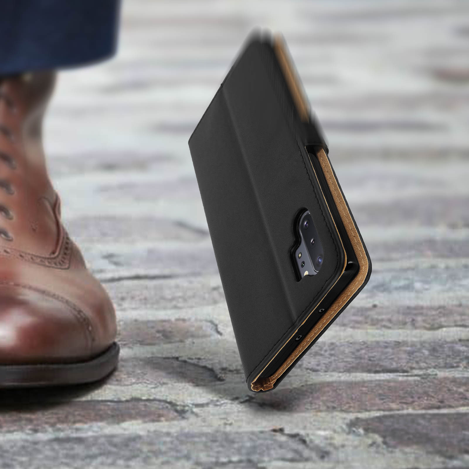 Chaussure en cuir marron et étui de téléphone noir sur dalles.
