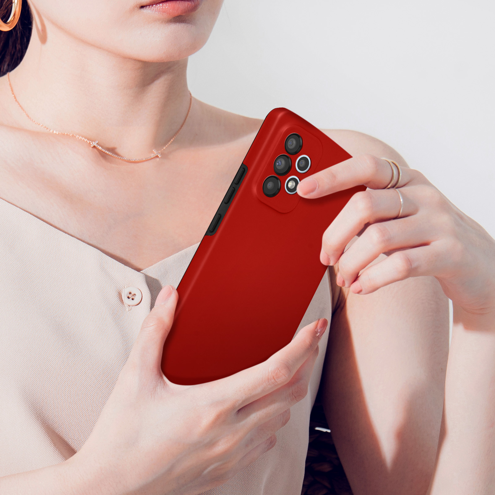 Une personne tient un smartphone rouge avec quatre caméras au dos.