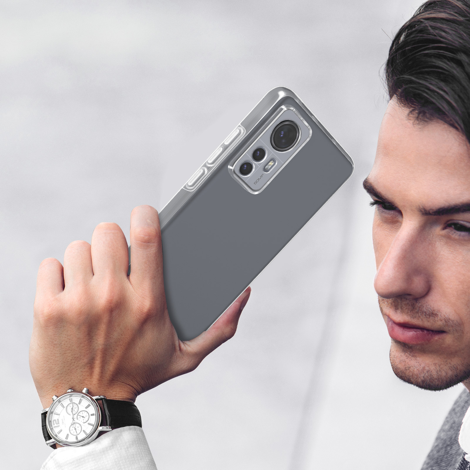 Homme avec montre tient un smartphone gris avec trois caméras.