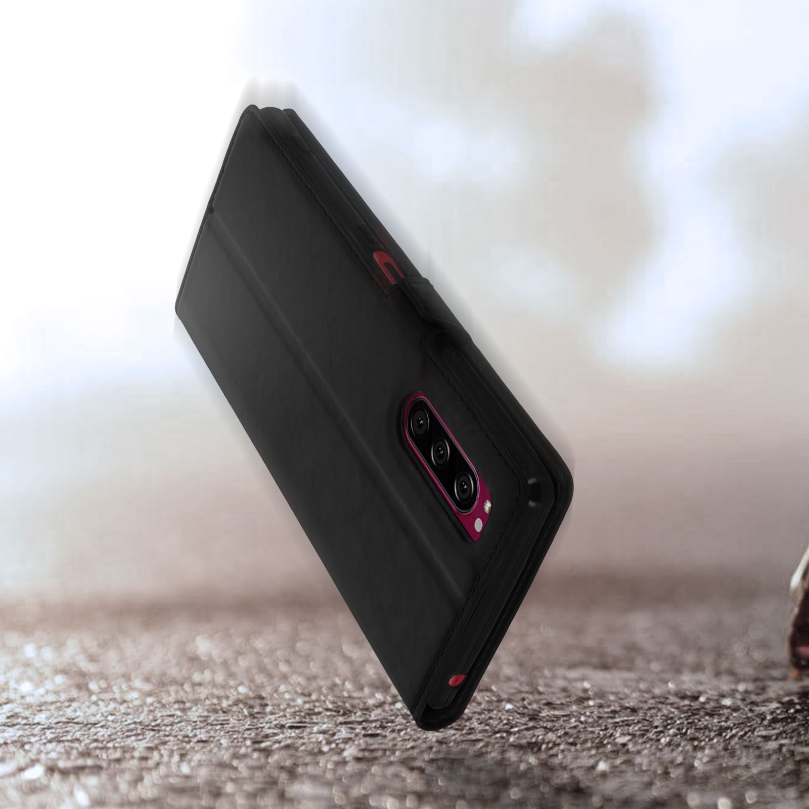 Una custodia a libro nera per smartphone con tre fotocamere poggia su superficie ruvida.
