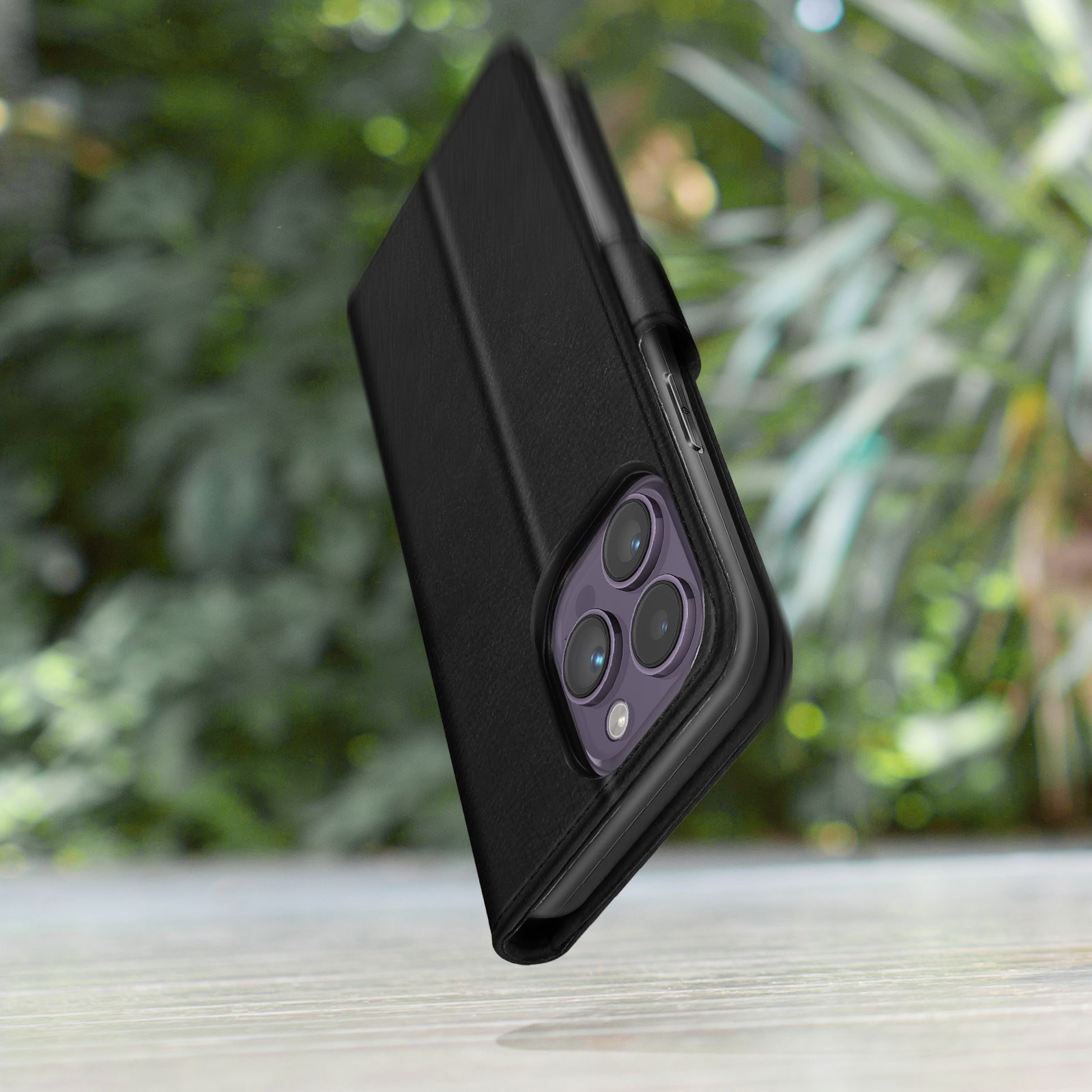 Telefono nero con custodia a libro e fotocamere su tavolo di legno con sfondo verde.