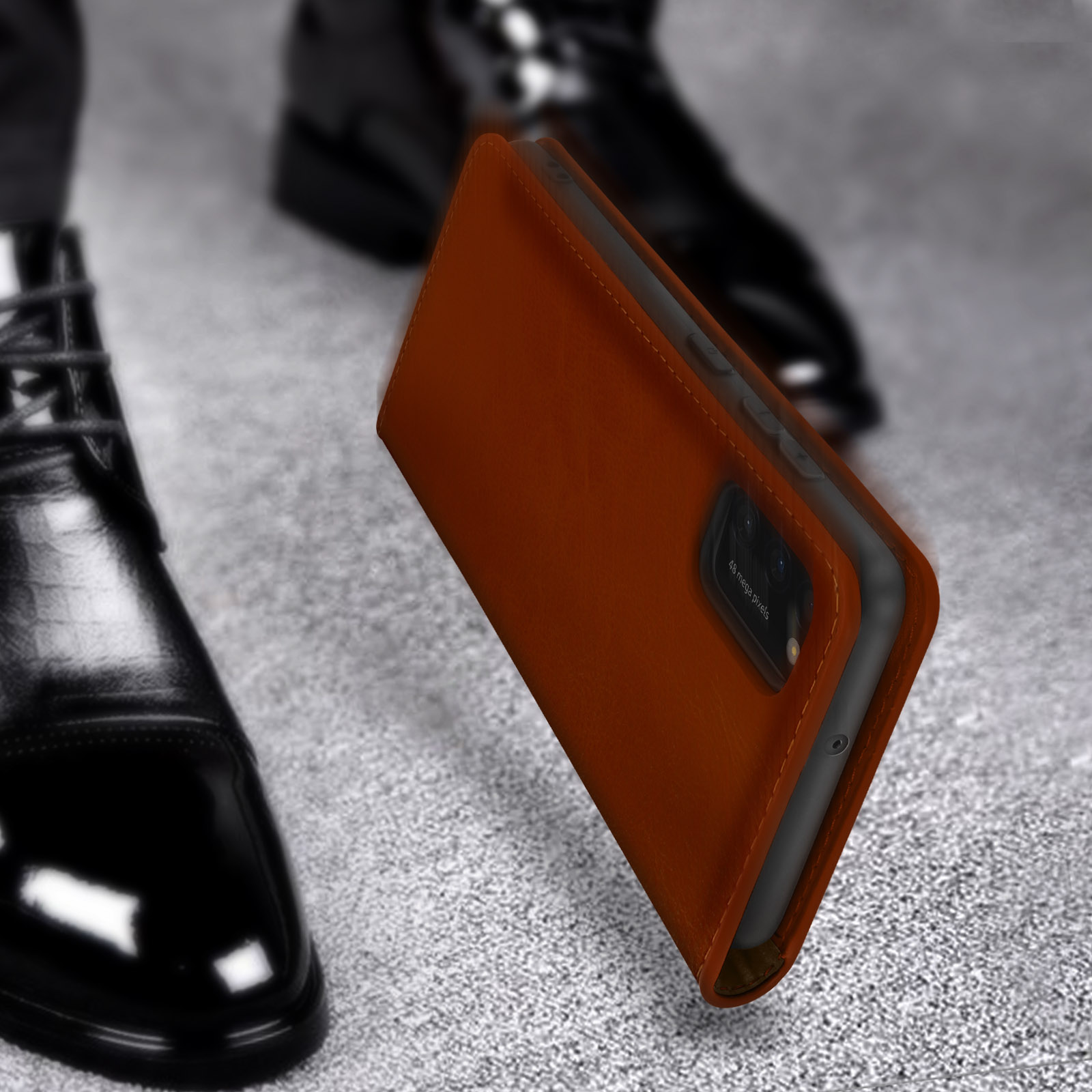 Un étui de téléphone en cuir marron repose sur une surface grise à côté de chaussures noires.
