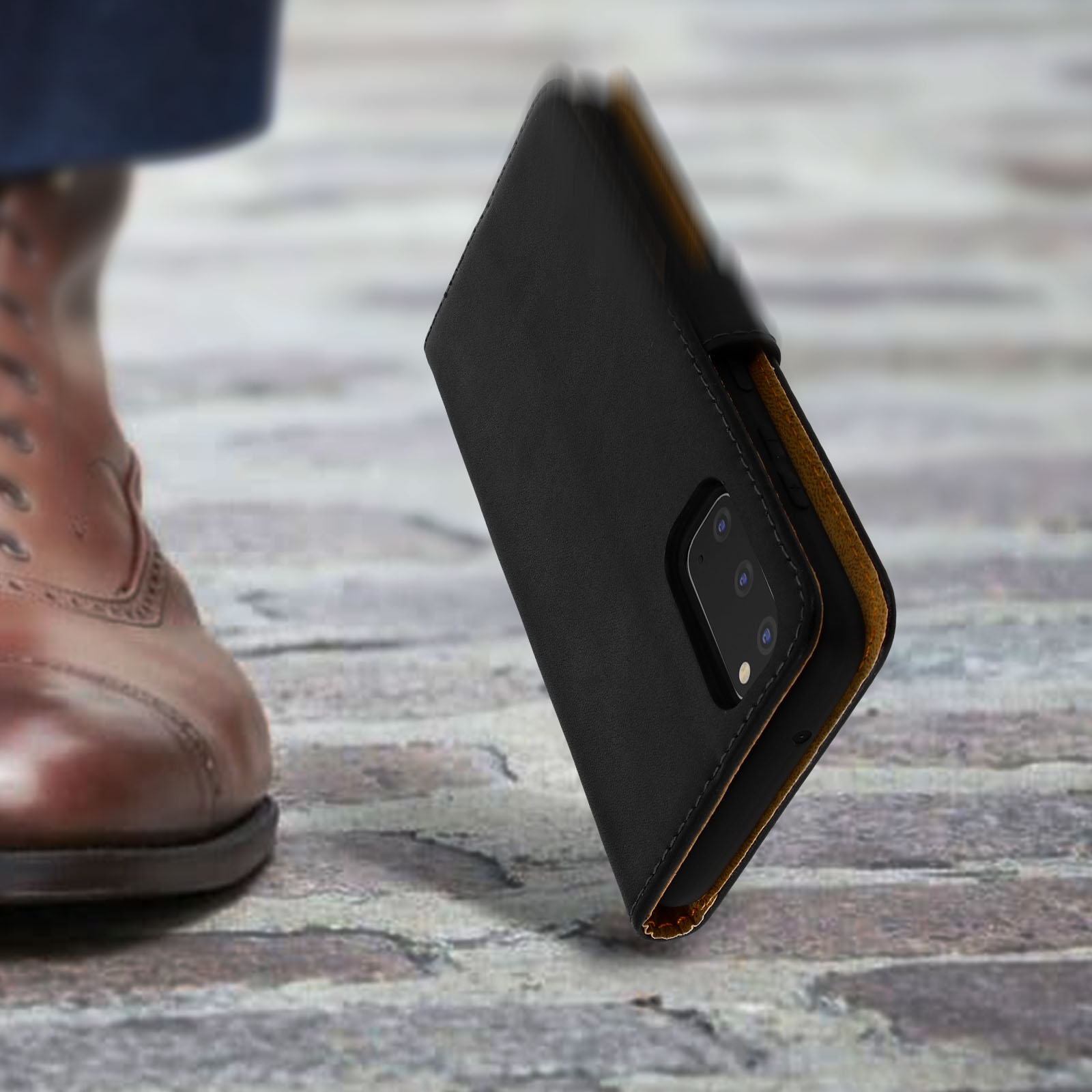 Een bruine leren schoen naast een zwarte telefoonhoes op kasseien.