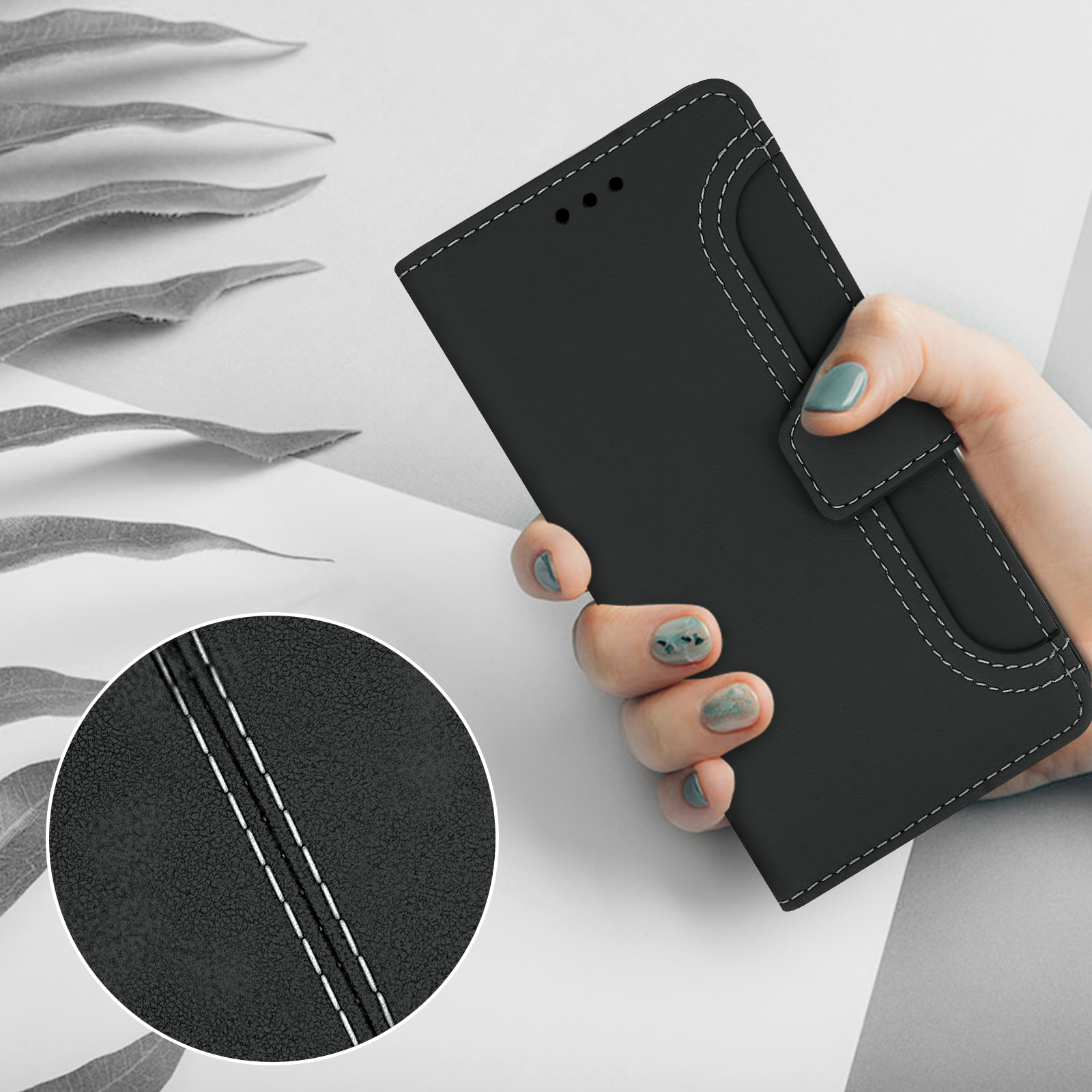Een hand houdt een zwarte telefoonhoes met witte stiksels vast tegen een bladdecoratie.