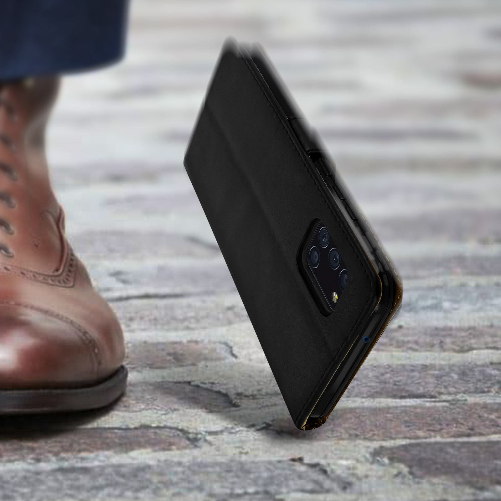 Scarpa marrone e cover a libro nera per telefono su sfondo acciottolato.