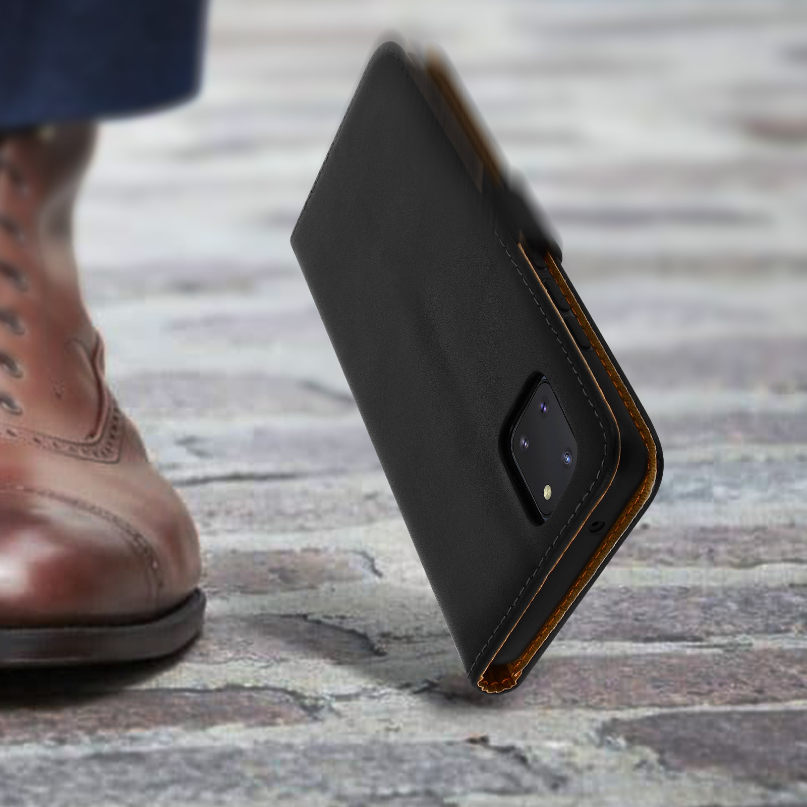Custodia nera per telefono cade su terreno acciottolato, scarpa in pelle marrone visibile.