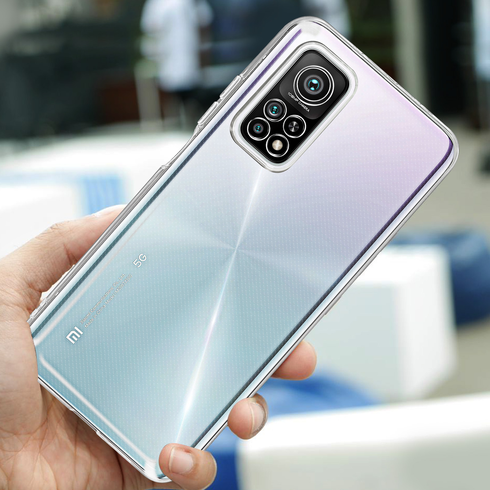 Una mano tiene un telefono trasparente con quattro fotocamere. Lo sfondo è sfocato.