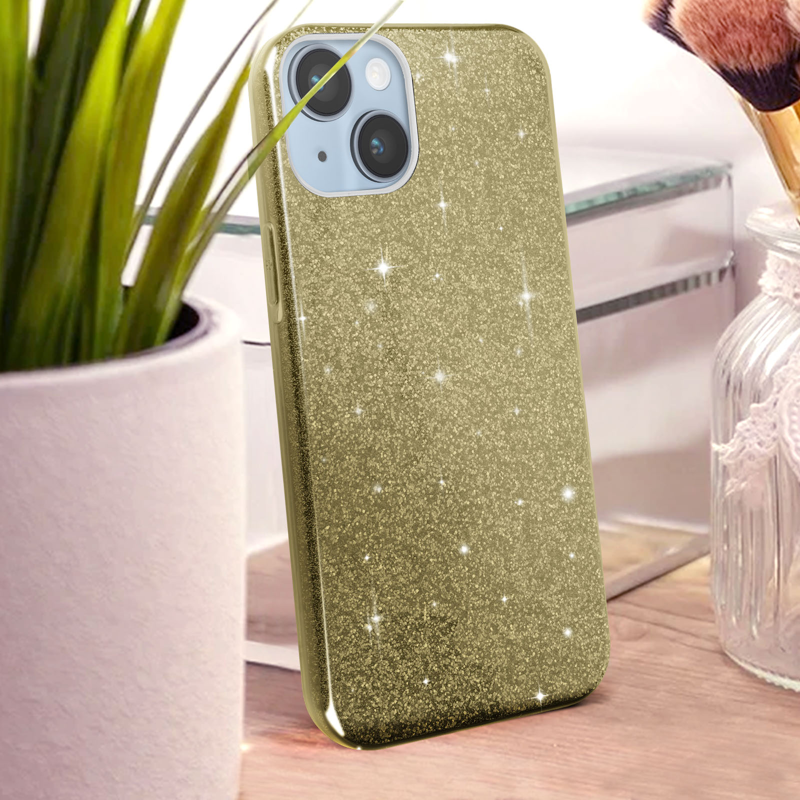 Coque de téléphone dorée à paillettes avec caméras sur table en bois et plantes.