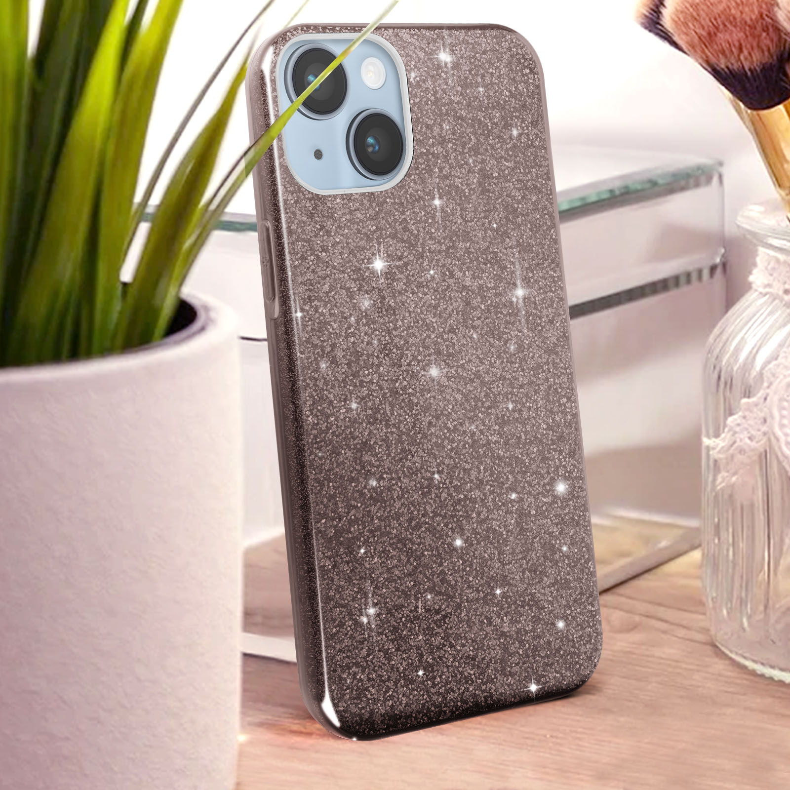 Une coque de téléphone rose doré à paillettes se dresse sur une table en bois près d'une plante.