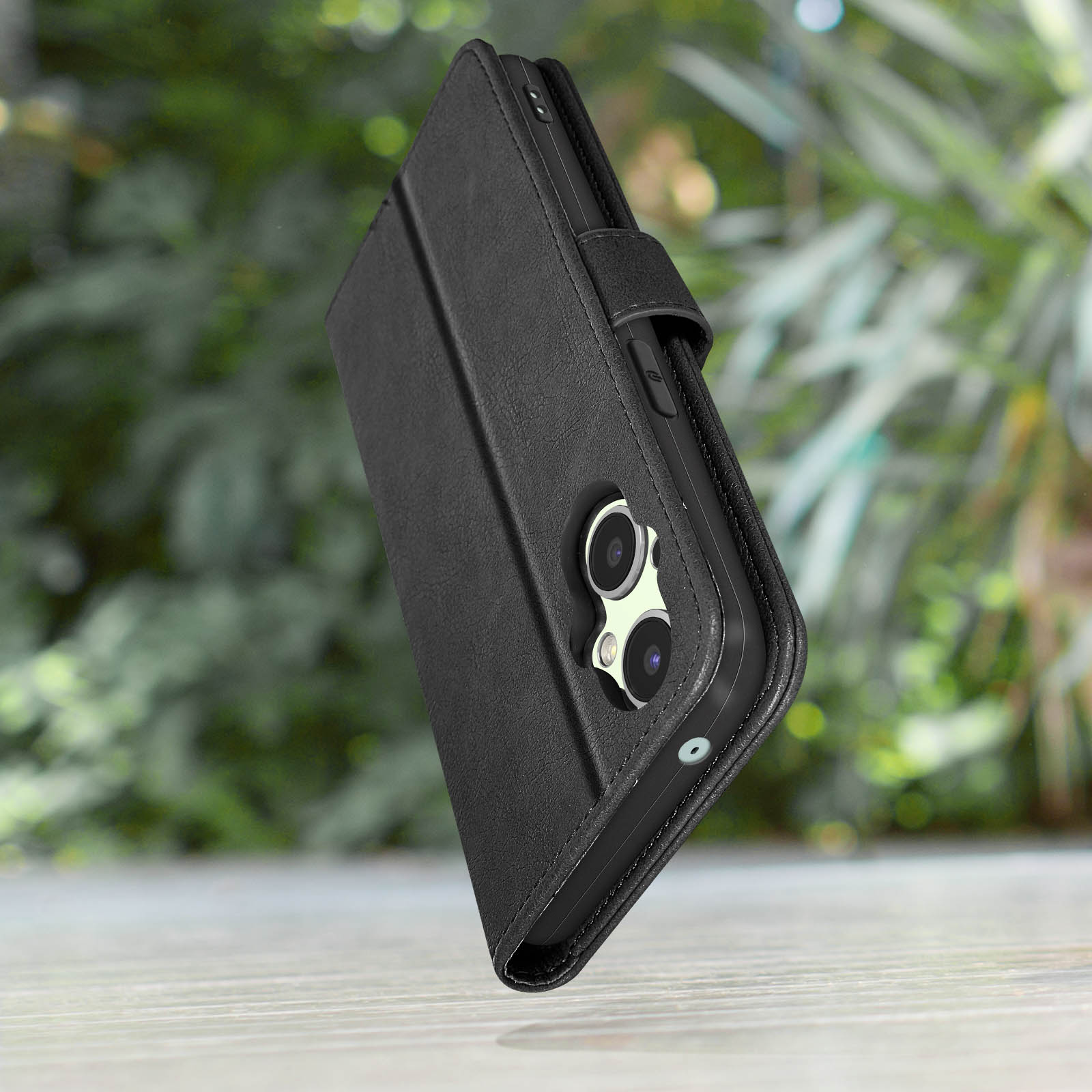 Custodia a libro nera per telefono con fotocamere su tavolo in legno, sfondo verde.