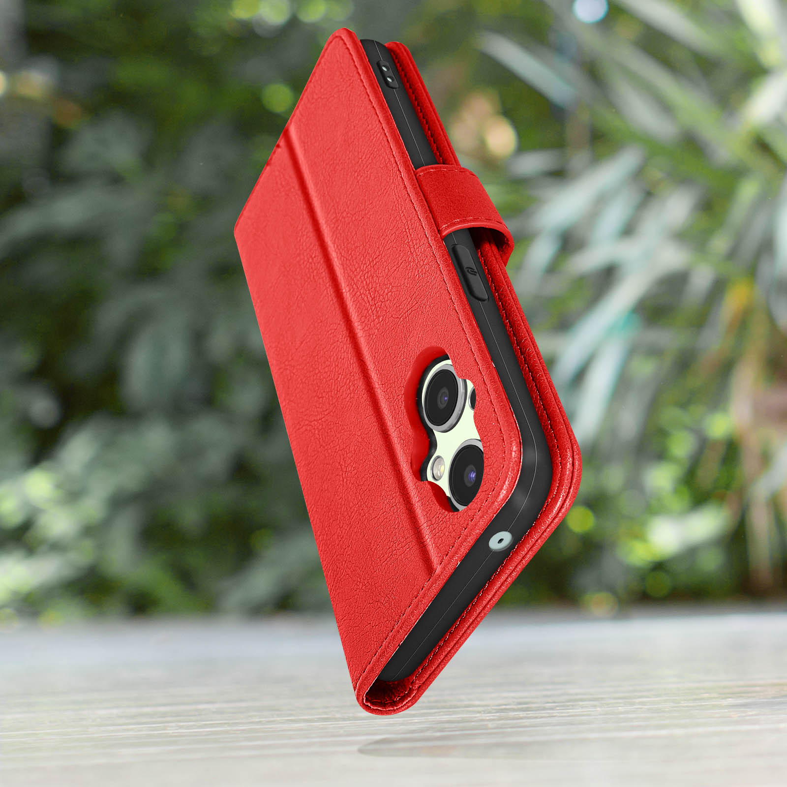 Custodia rossa per telefono con fotocamere su tavolo di legno con sfondo verde sfocato.