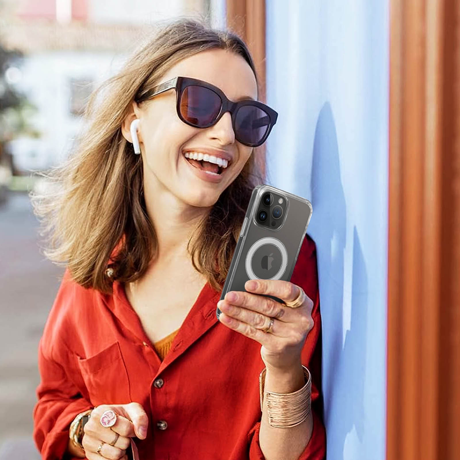 Vrouw met zonnebril en oordopjes lacht, houdt telefoon met hoesje vast.