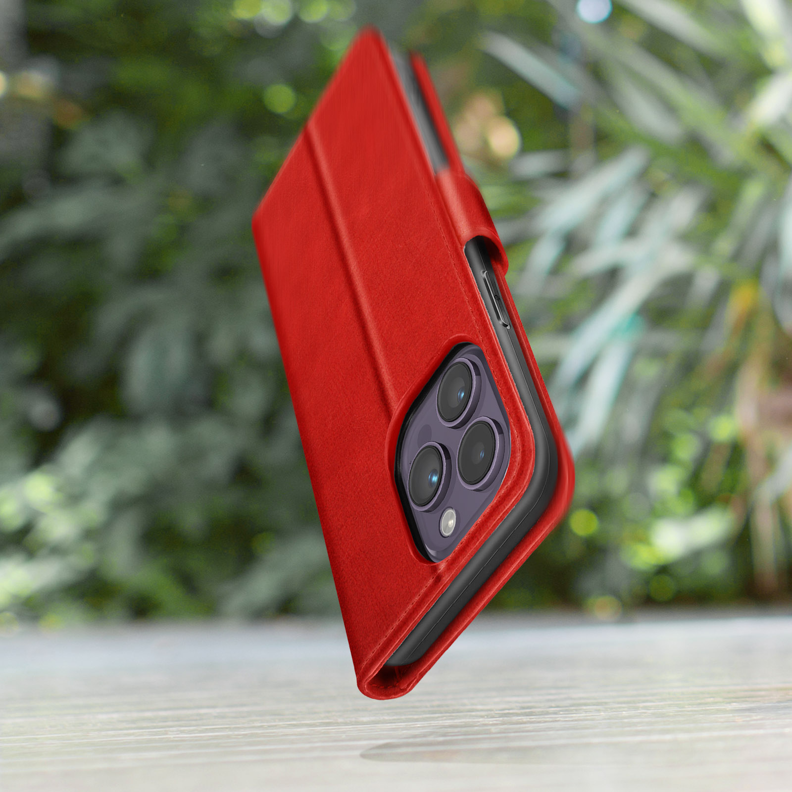 Un étui de téléphone rouge avec trois objectifs d'appareil photo sur fond vert flou.