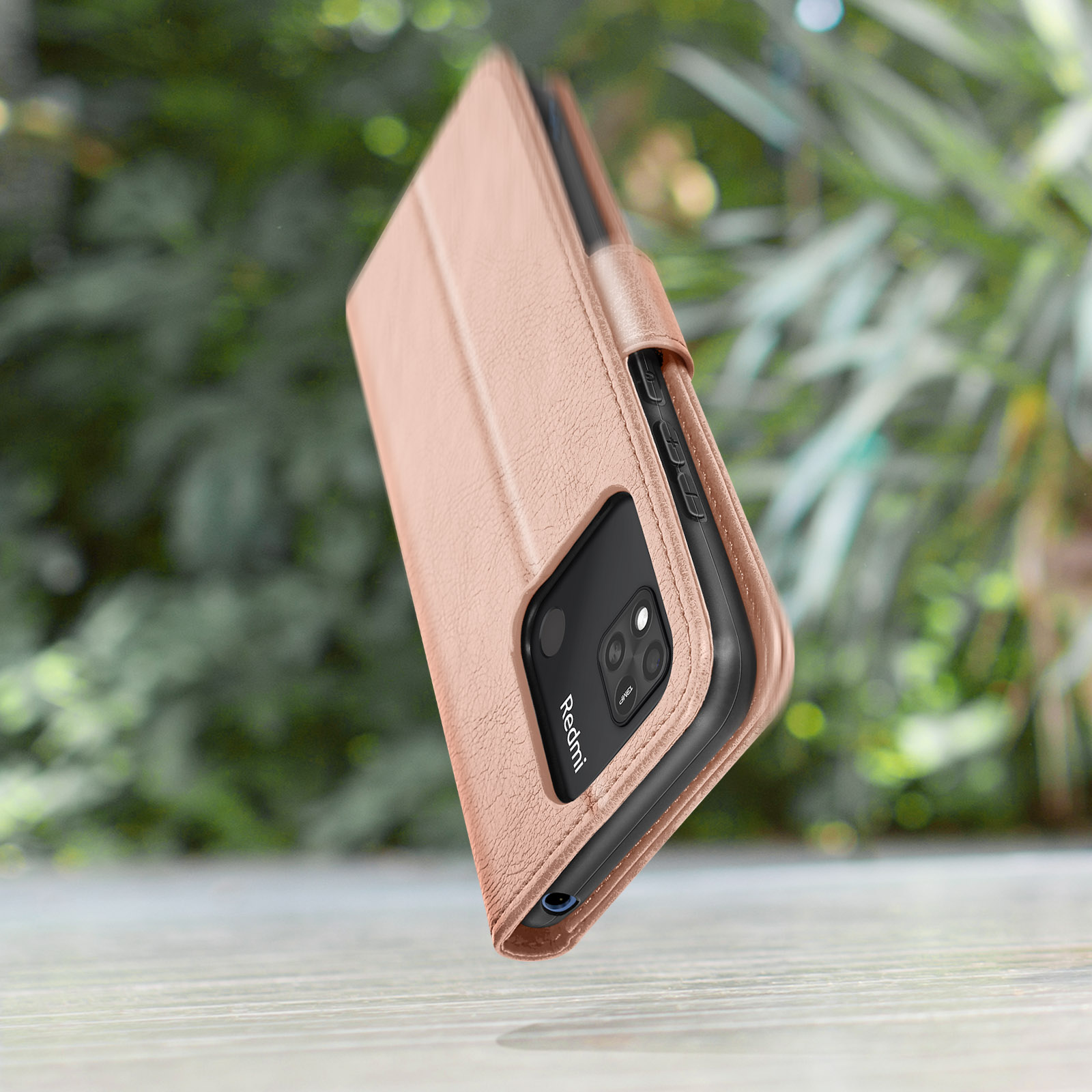 Una custodia per telefono color oro rosa poggia su un tavolo di legno, con vegetazione sfocata sullo sfondo.