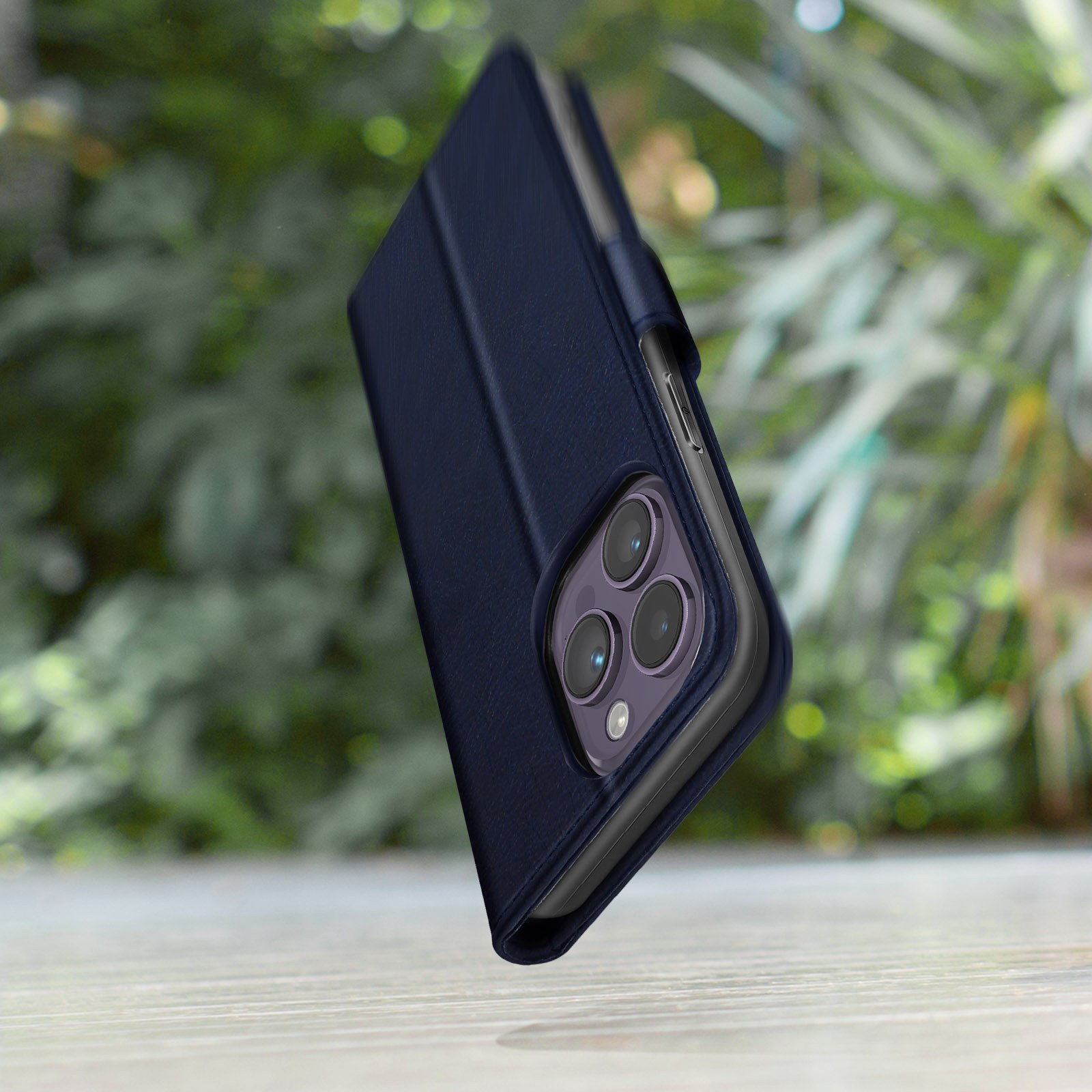 Étui de téléphone bleu foncé avec trois caméras, devant un feuillage vert.