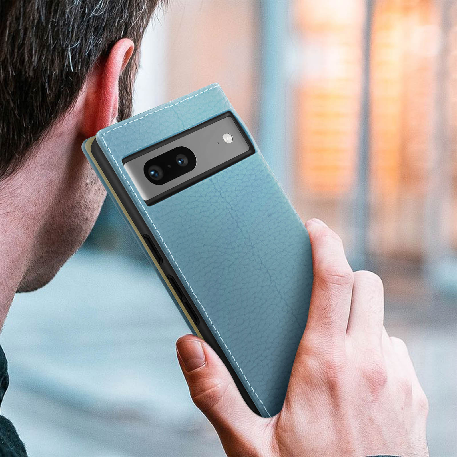 Man houdt een blauwe telefoon met twee camera's vast, oor is zichtbaar.