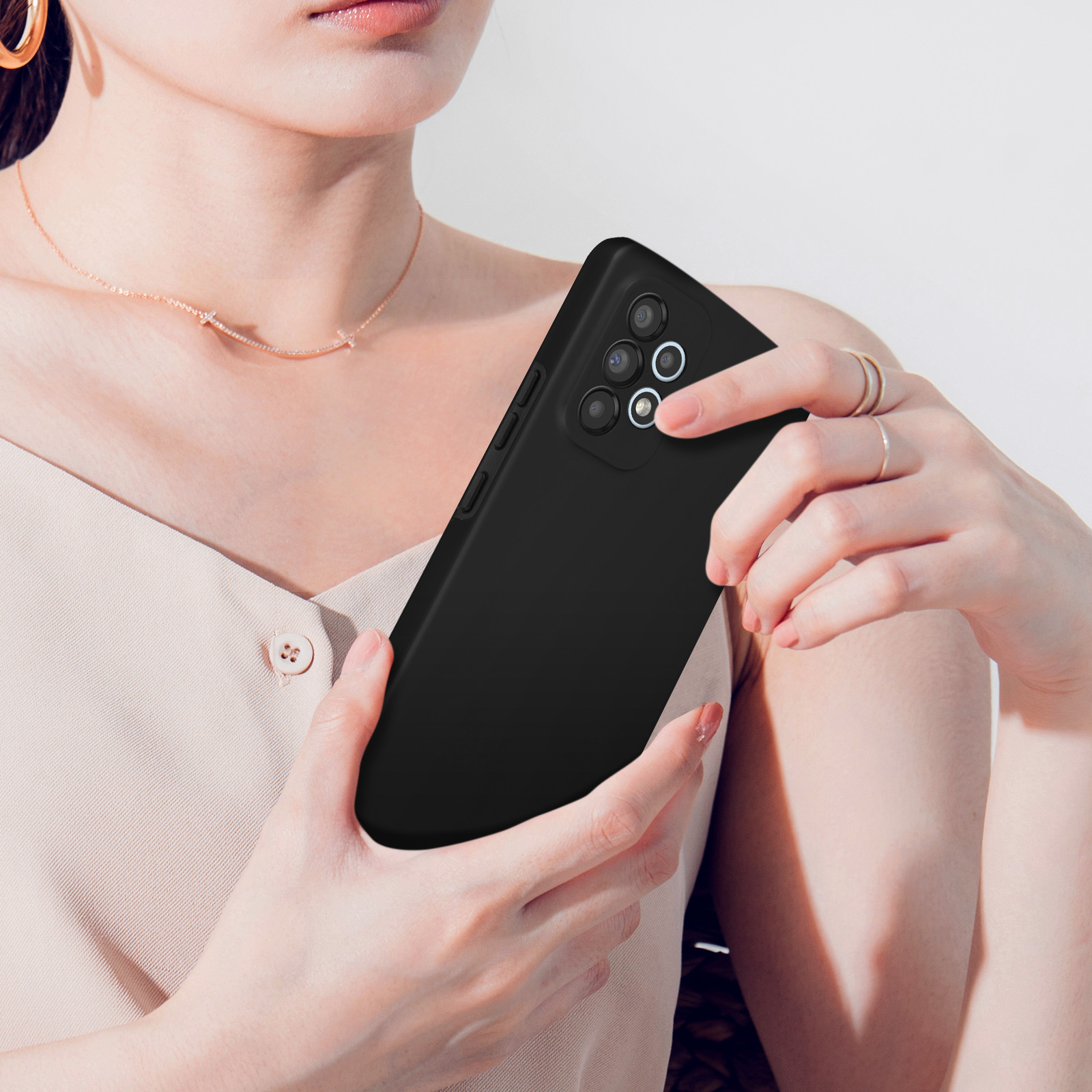Une femme tient un smartphone noir à quatre caméras, posé sur son torse.