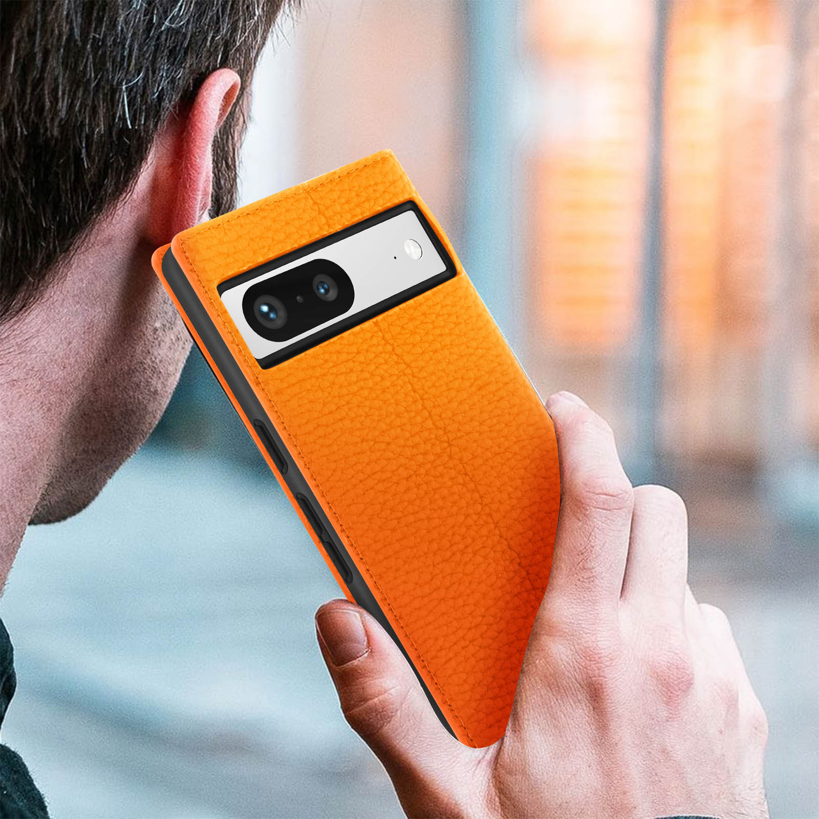 Oranje telefoonhoesje met cameralens bij oor gehouden door een hand.