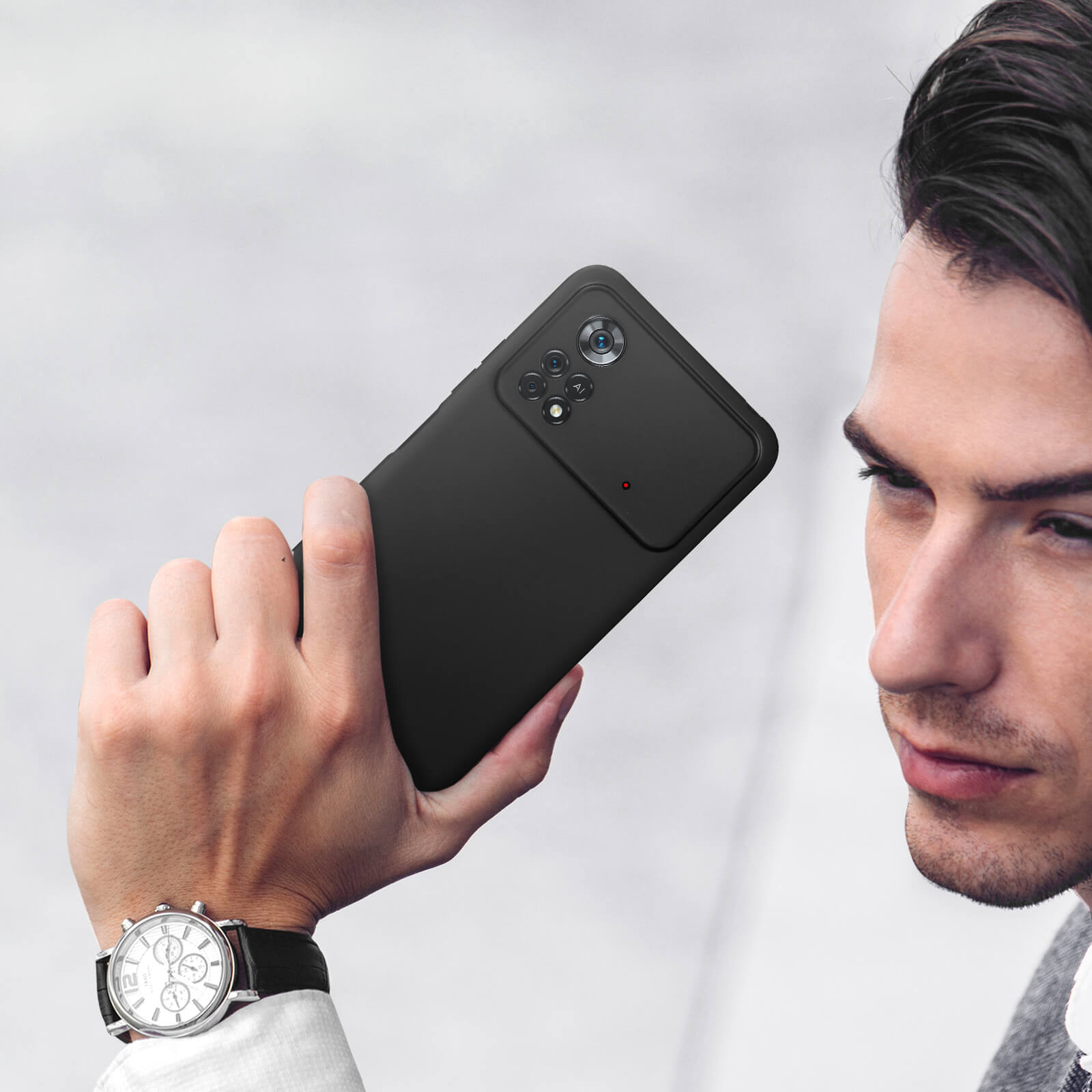 Un homme tient un smartphone noir avec quatre caméras et un point rouge.