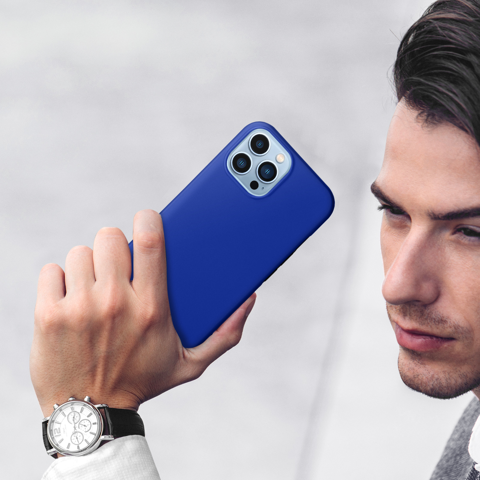 Man houdt een blauwe smartphone met drievoudige camera vast. Polshorloge zichtbaar.