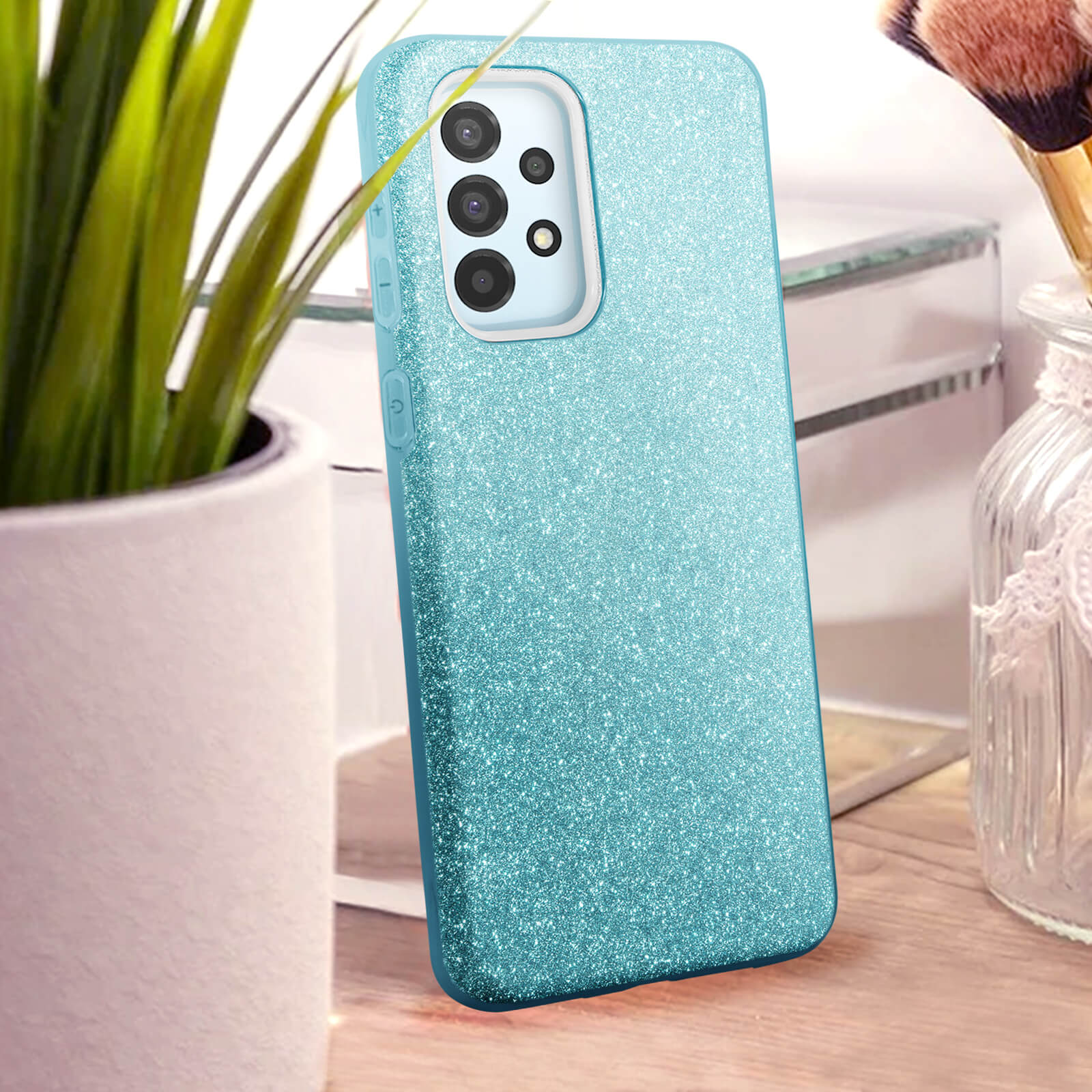Une coque de téléphone turquoise scintillante à côté d'une plante et de pinceaux.