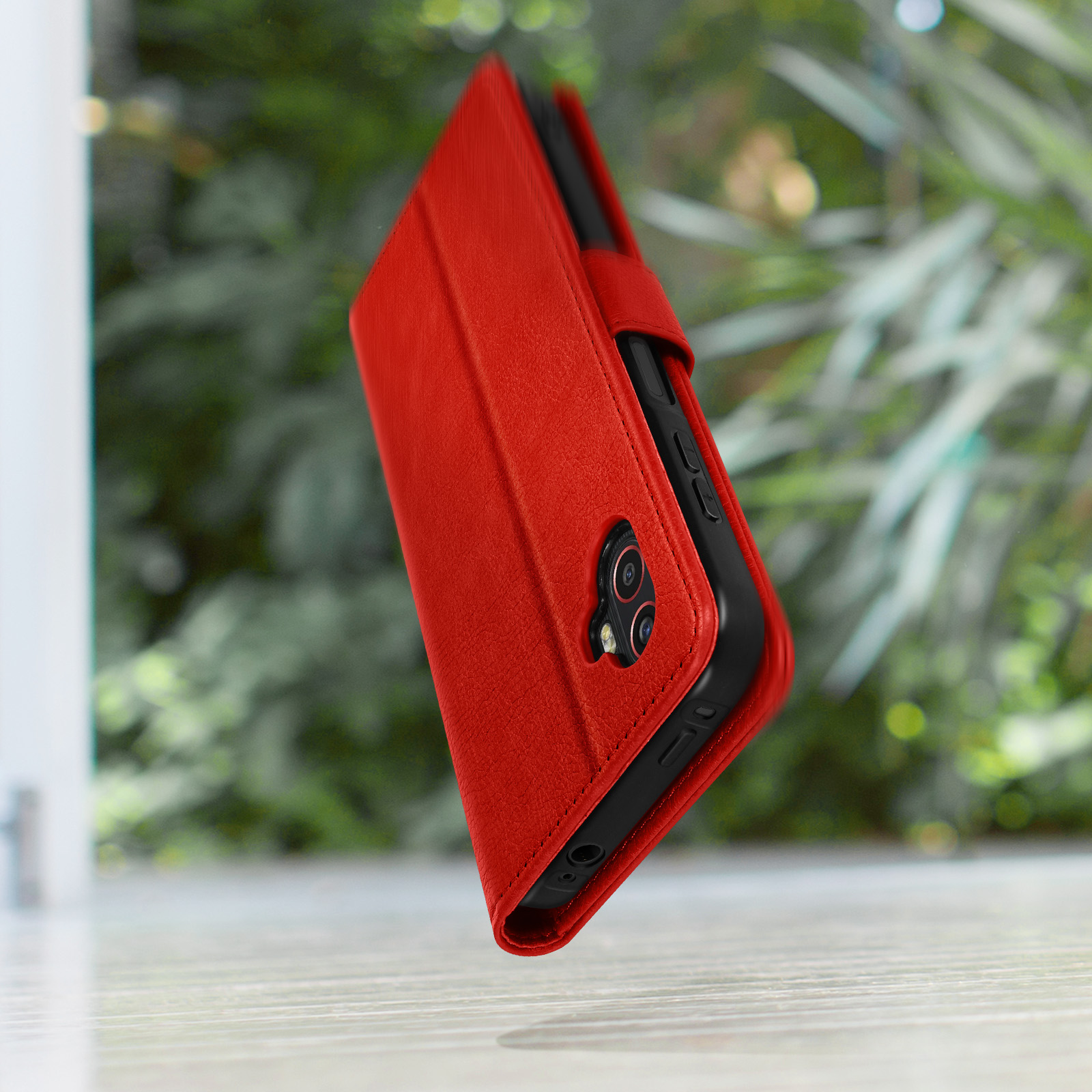 Étui rouge en cuir pour téléphone avec caméras et boutons nets, arrière-plan flou.