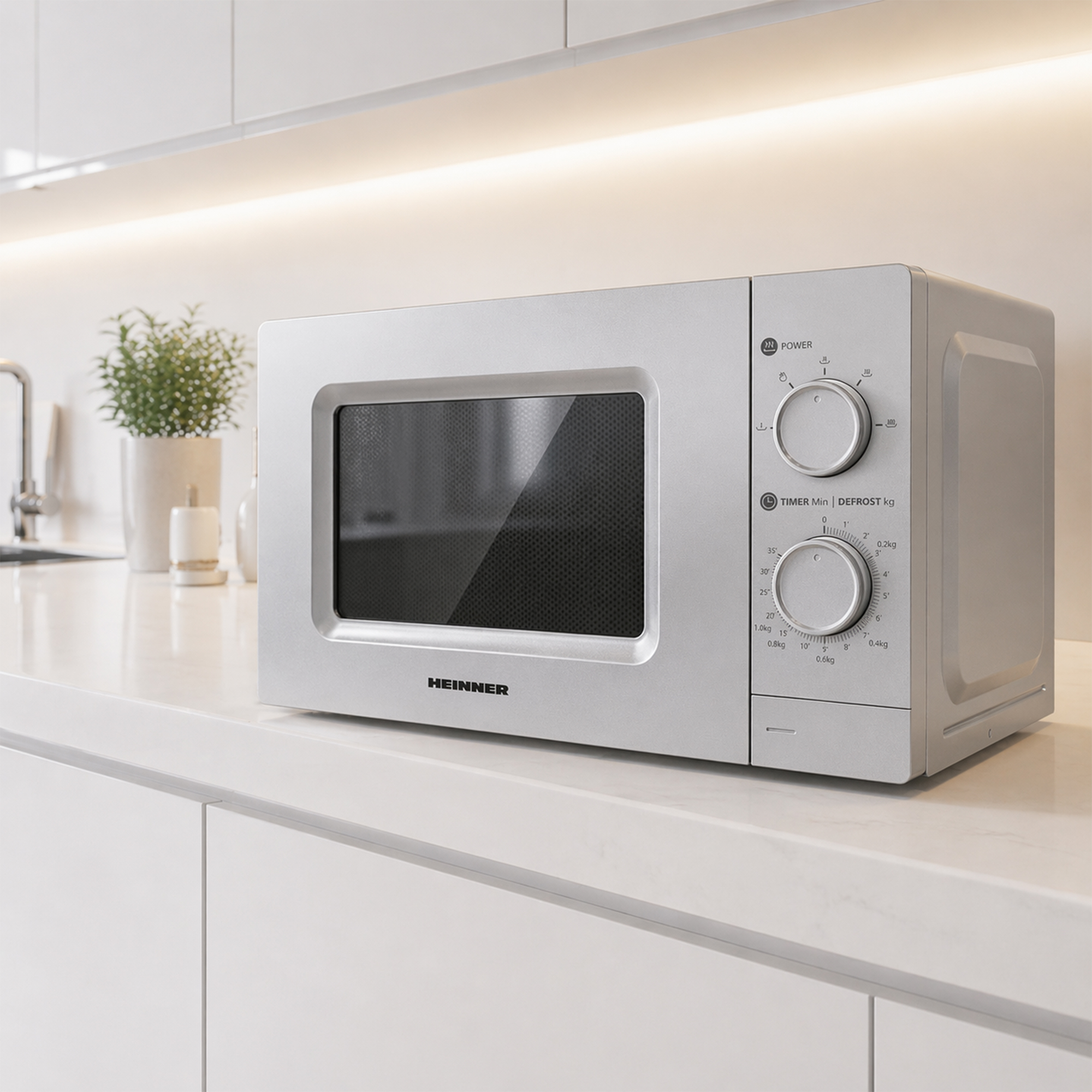 A silver Heinner microwave sits on a white countertop next to a potted plant.