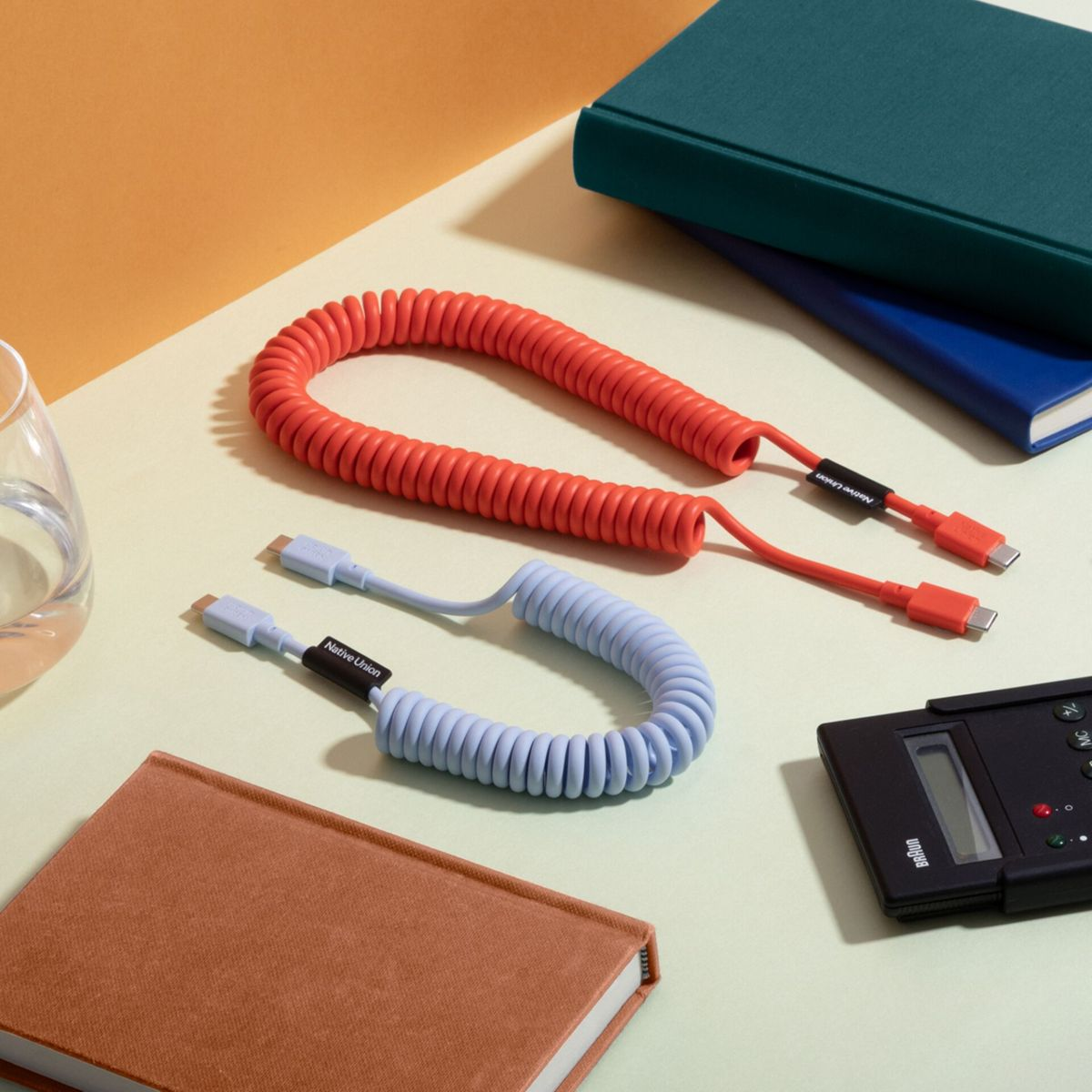 Des câbles USB-C orange et bleus enroulés reposent sur un bureau avec des livres et une calculatrice.