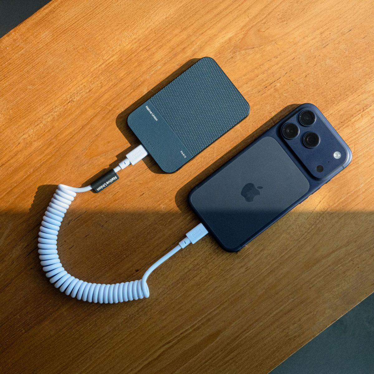 Un iPhone bleu est en charge via un câble blanc torsadé depuis une banque d'alimentation bleue.