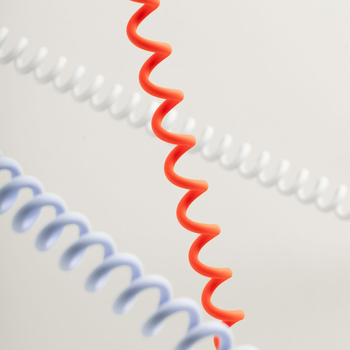 Trois cordons spiralés : orange, bleu et blanc, sur fond clair.