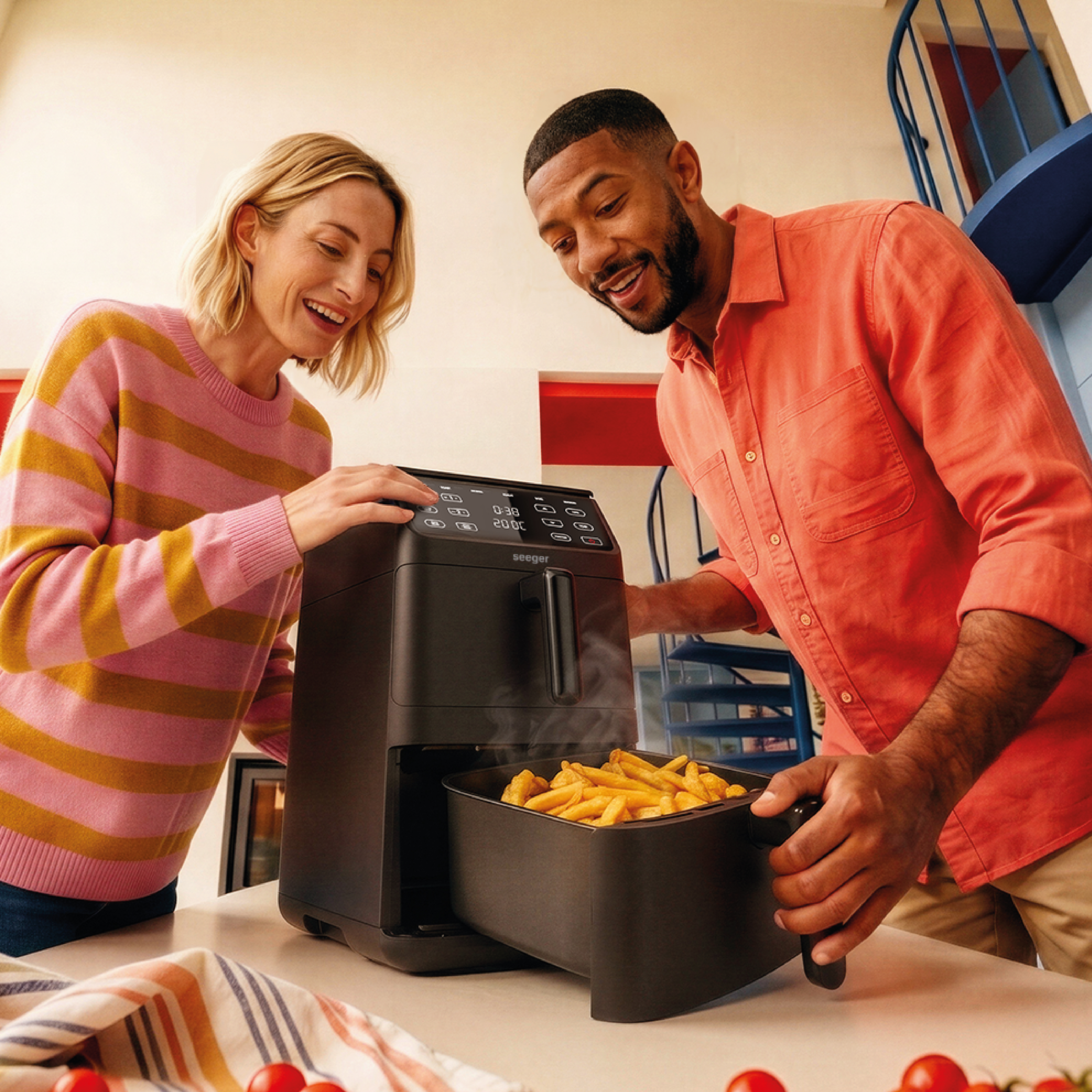 A man and woman look at an air fryer with french fries inside.