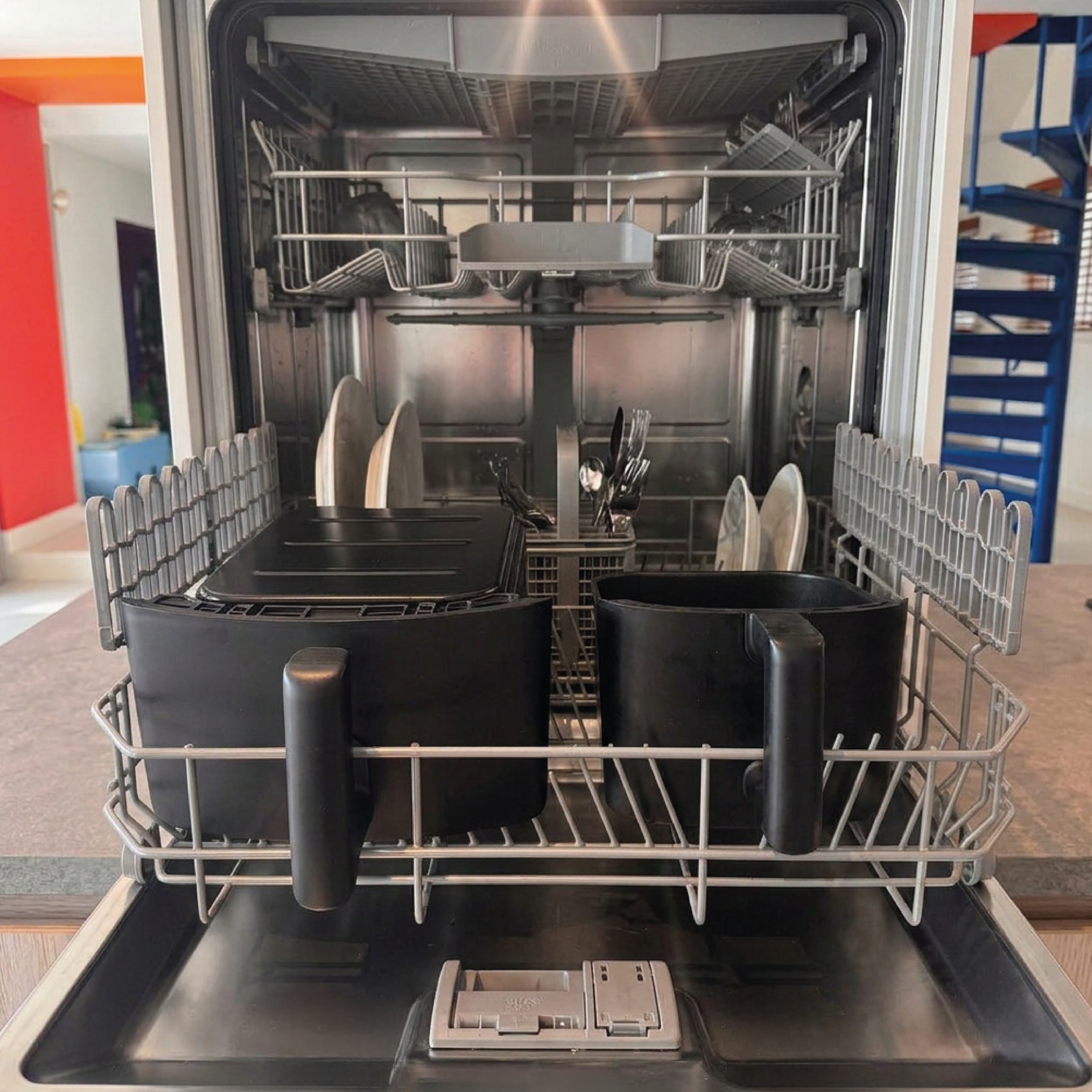 An open dishwasher with two black air fryers in the bottom rack.