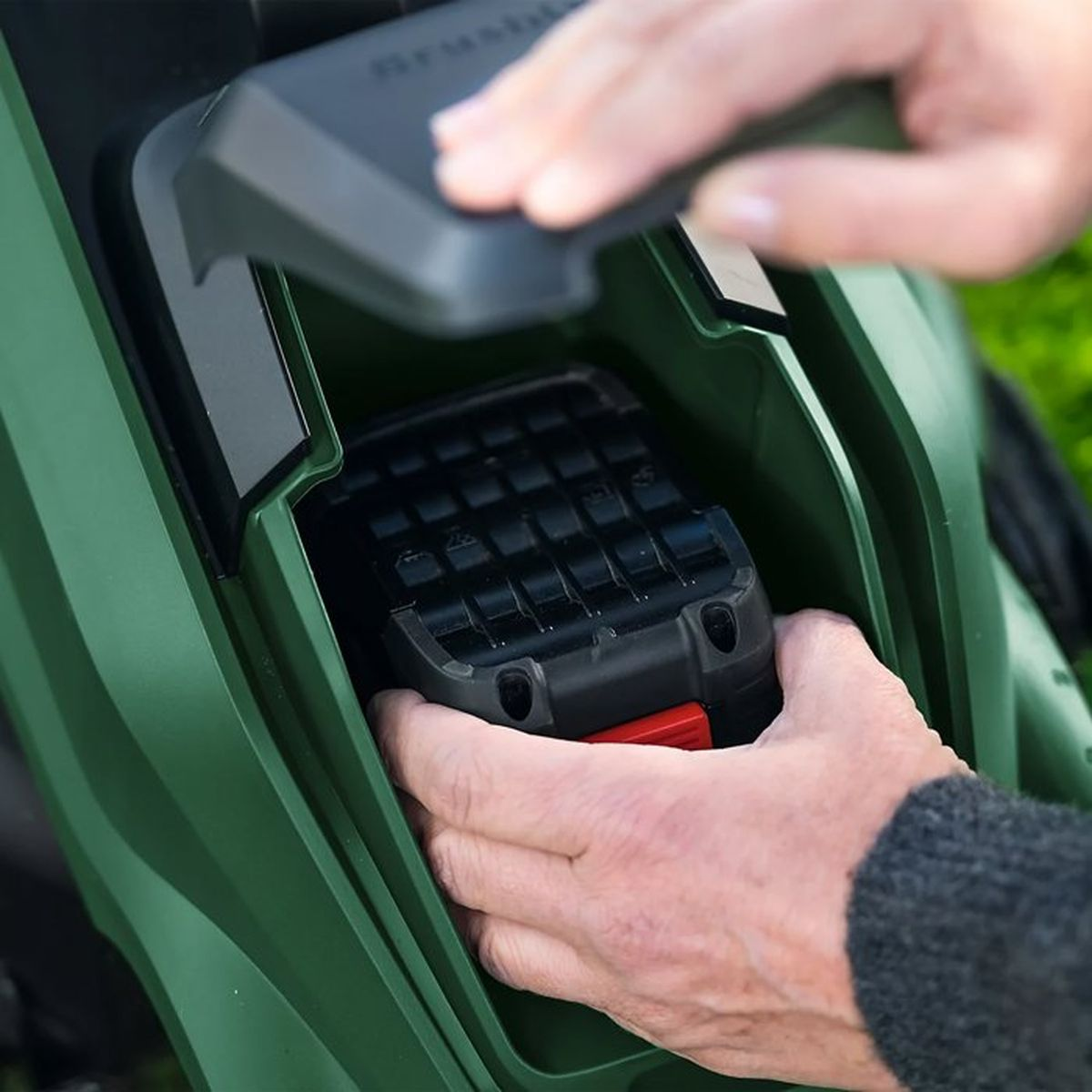 Hände setzen eine schwarze Batterie in ein grünes Gerät ein.