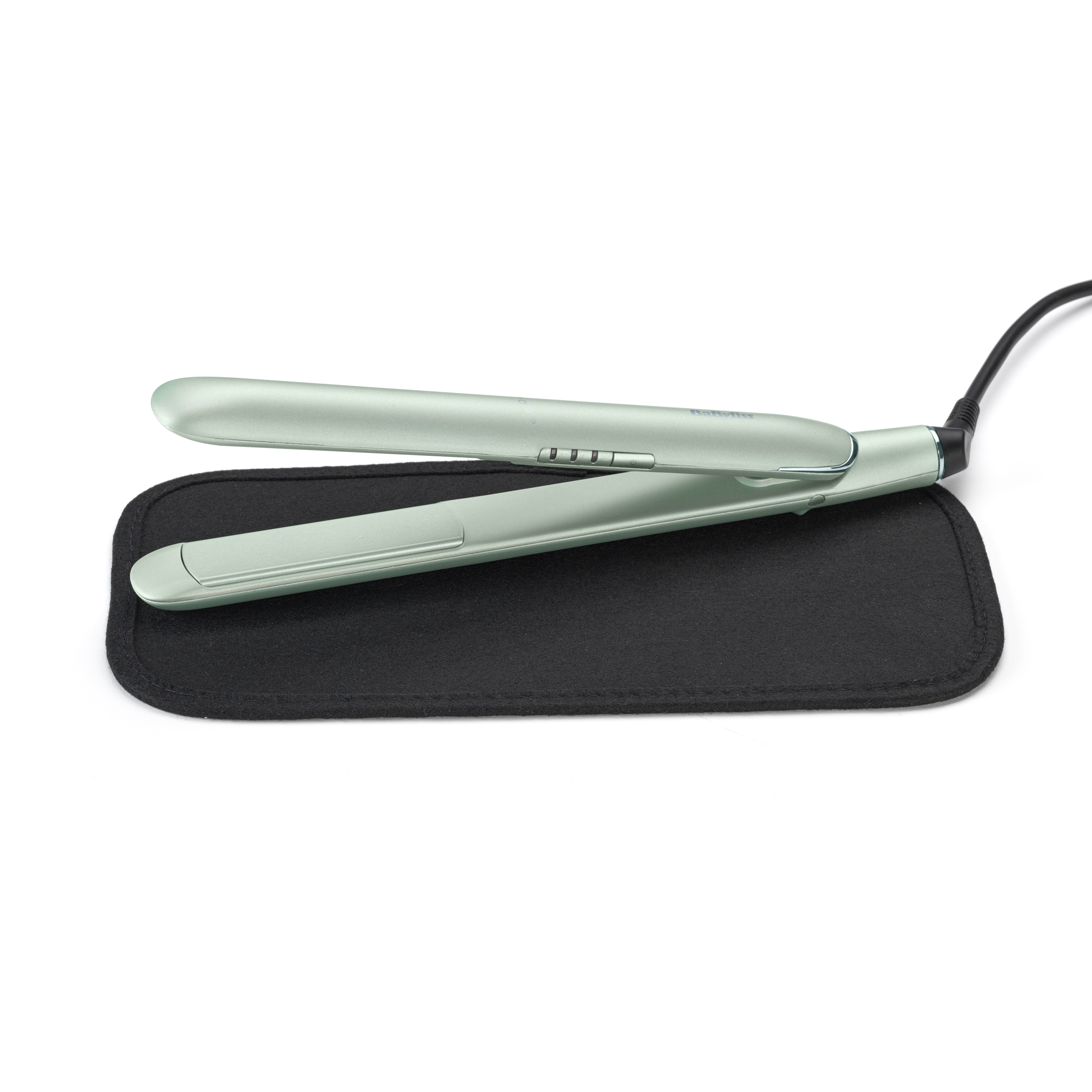 A green hair straightening iron rests on a black heat-resistant mat.