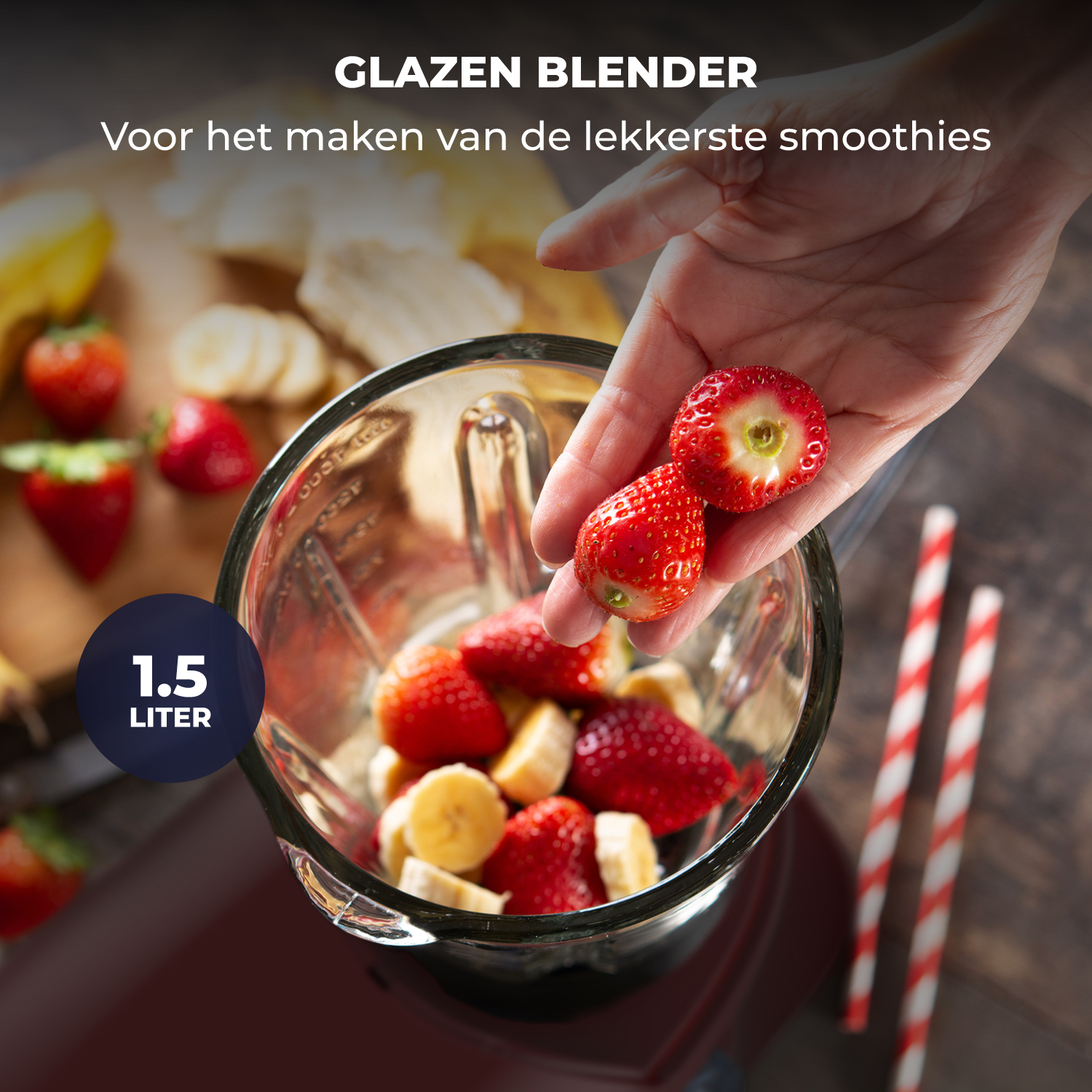 A hand adds strawberries and bananas to a glass blender, 1.5 liter capacity.