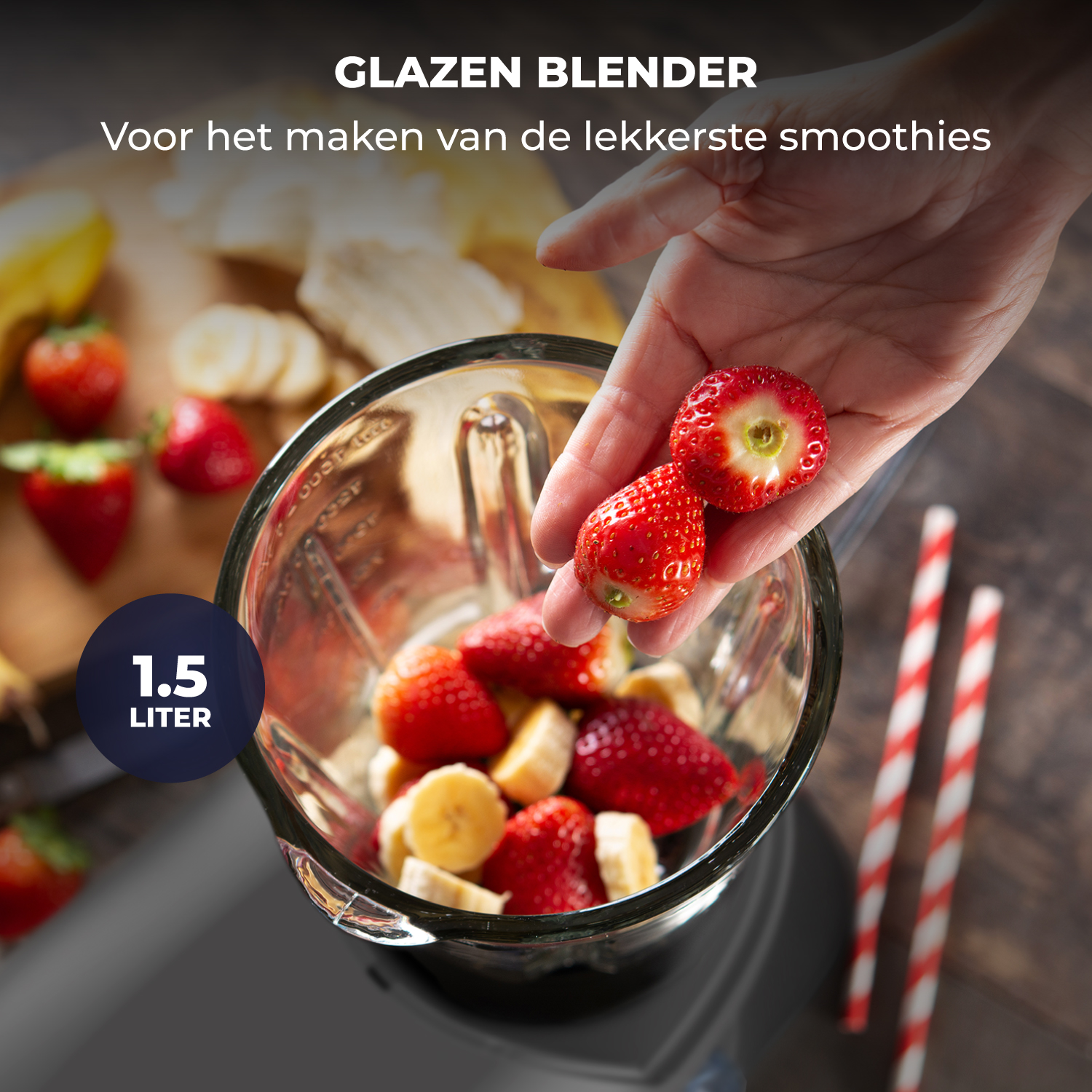 A hand adds strawberries and banana slices to a glass blender.