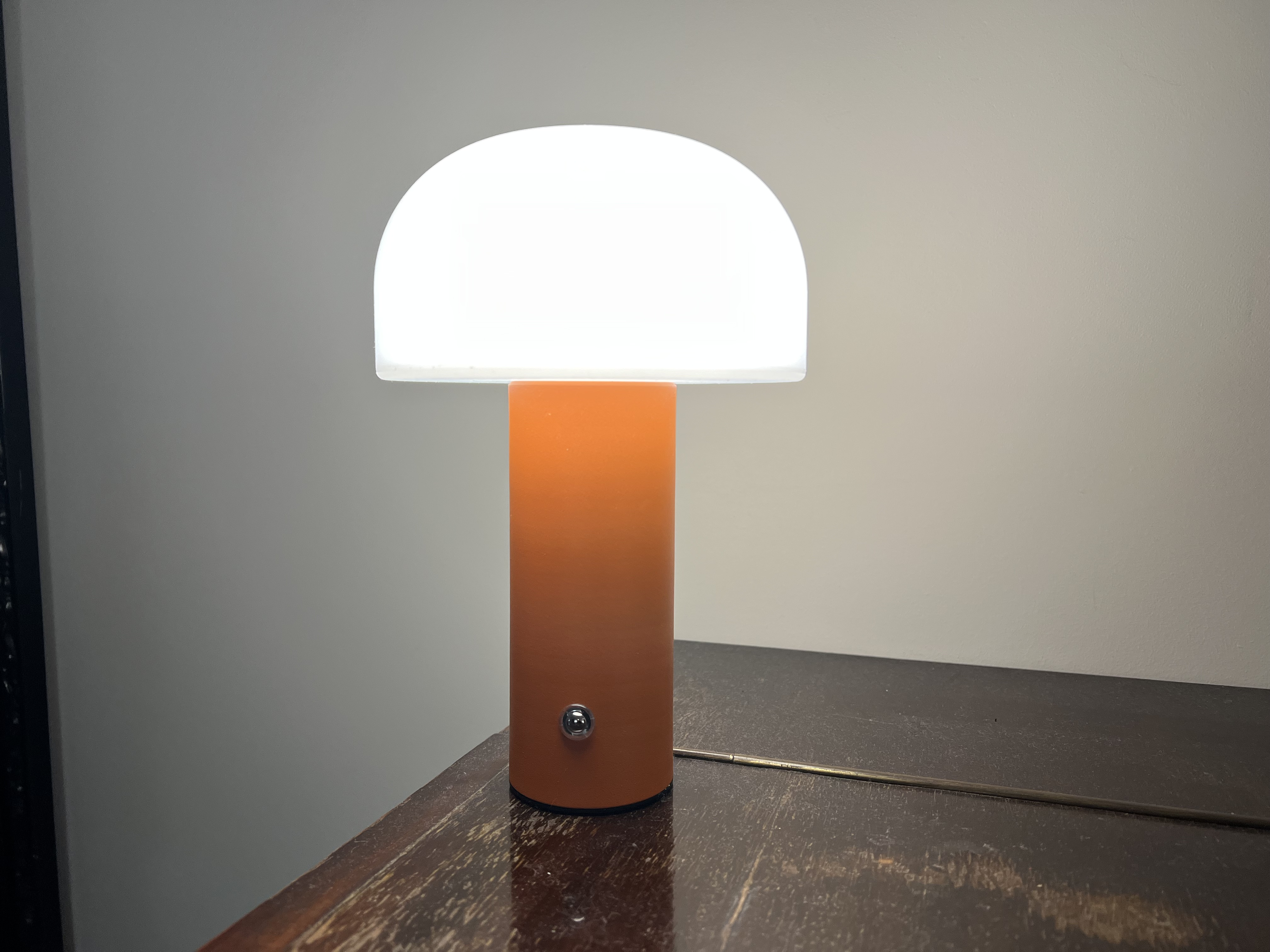 Eine orangefarbene pilzförmige Tischlampe mit weißer Kuppel steht auf einem dunklen Holztisch.