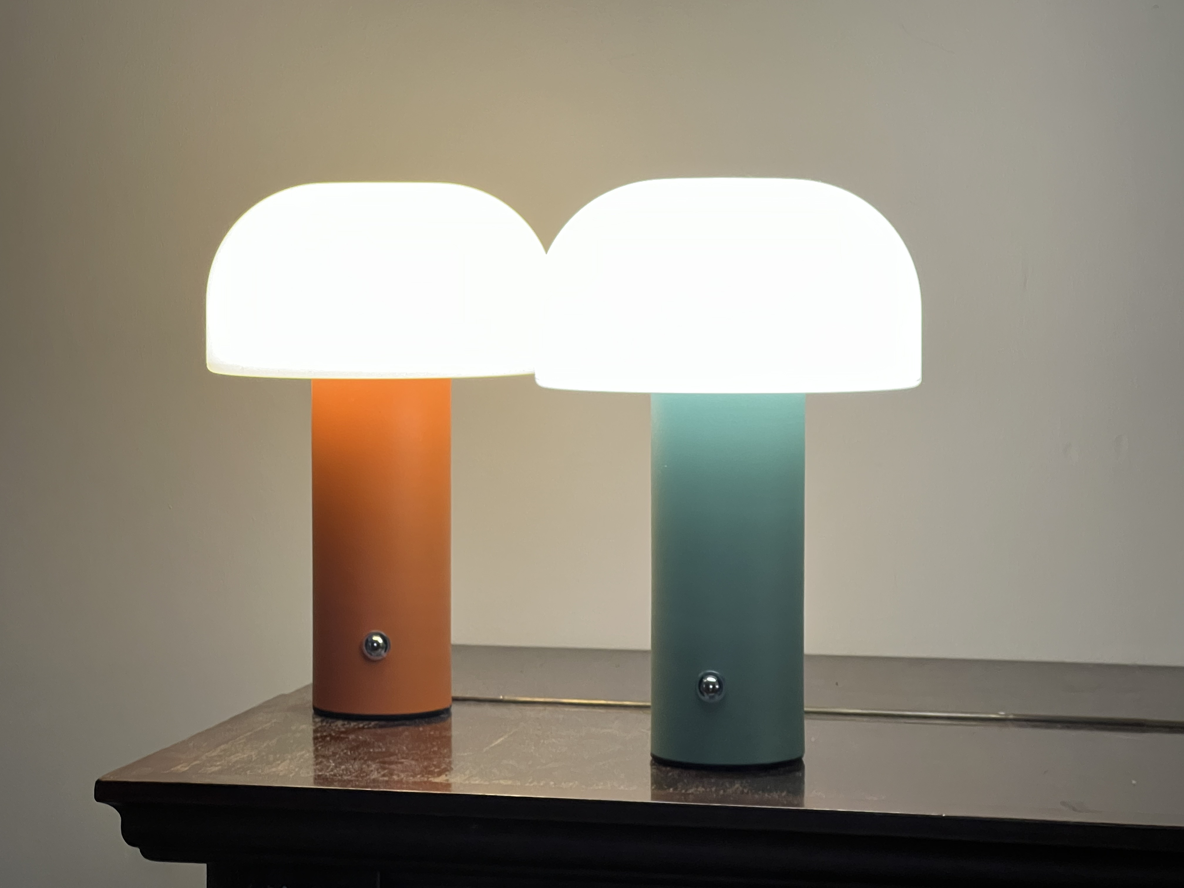Zwei Pilzlampen, eine orange und eine türkis, auf einem dunklen Tisch.