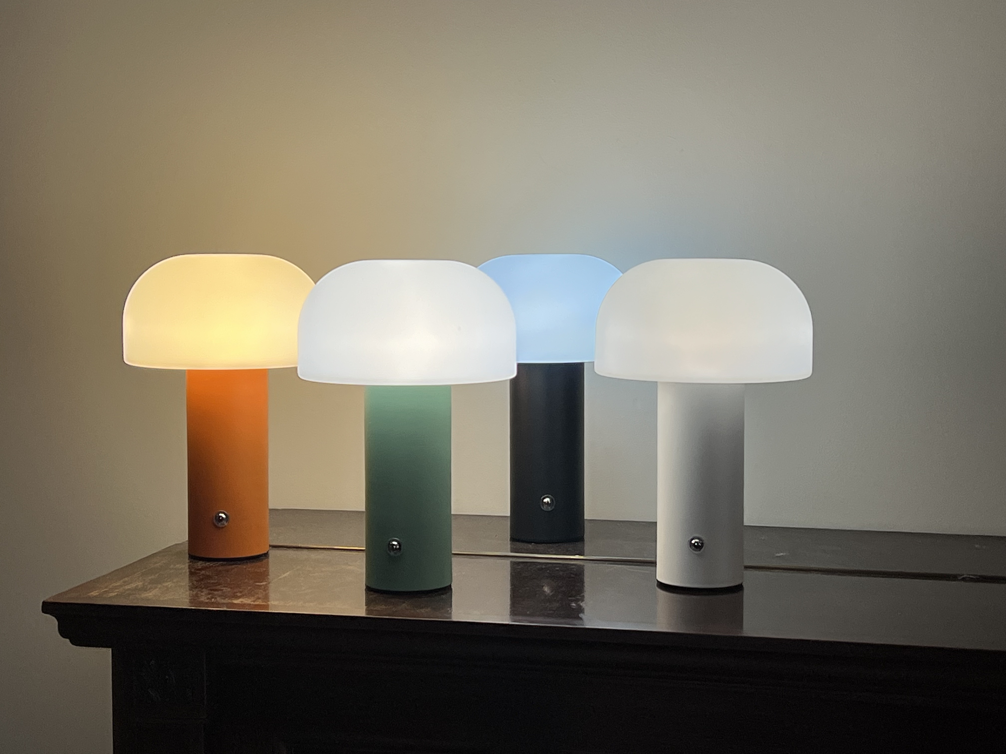 Vier Pilzförmige Lampen in Orange, Grün, Schwarz und Weiß auf einem Tisch.