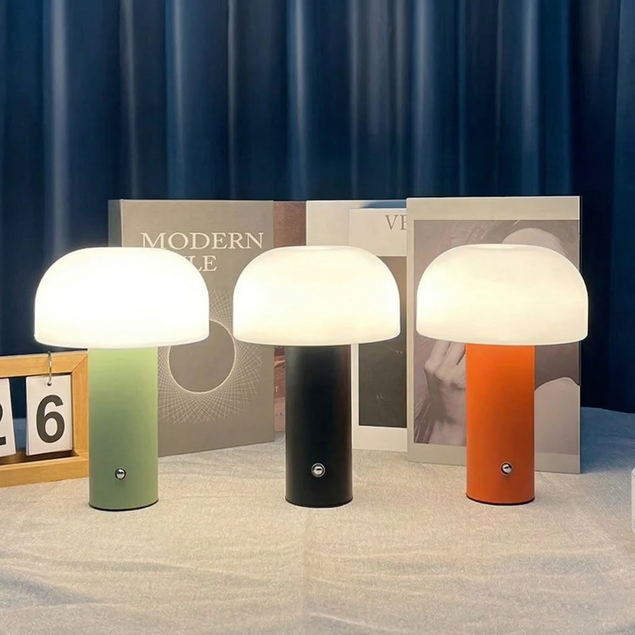 Drei Pilzförmige Tischlampen in Grün, Schwarz und Orange vor Büchern.