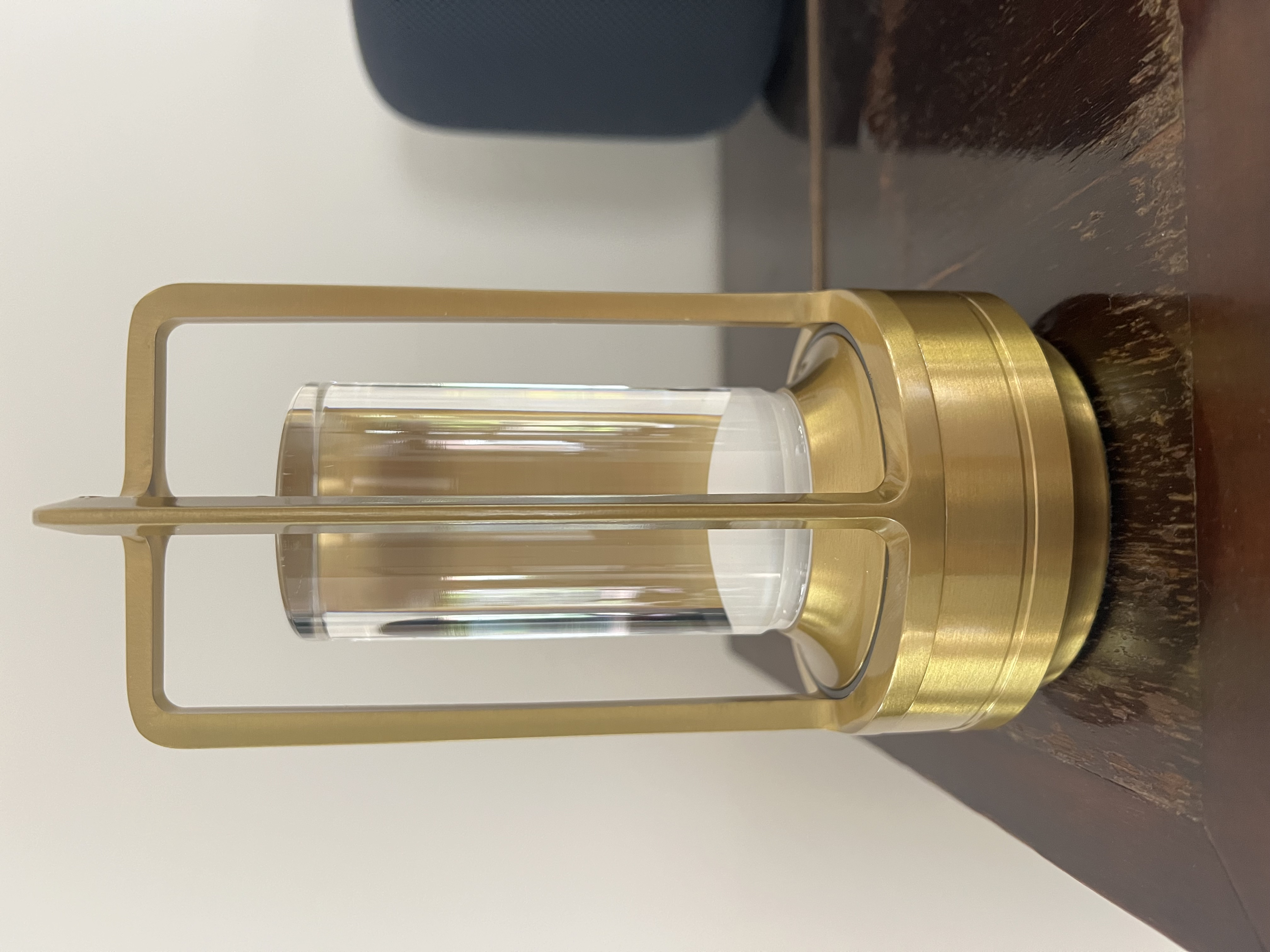 Eine goldene Lampe mit zylindrischem Glasbehälter auf einem Holztisch.