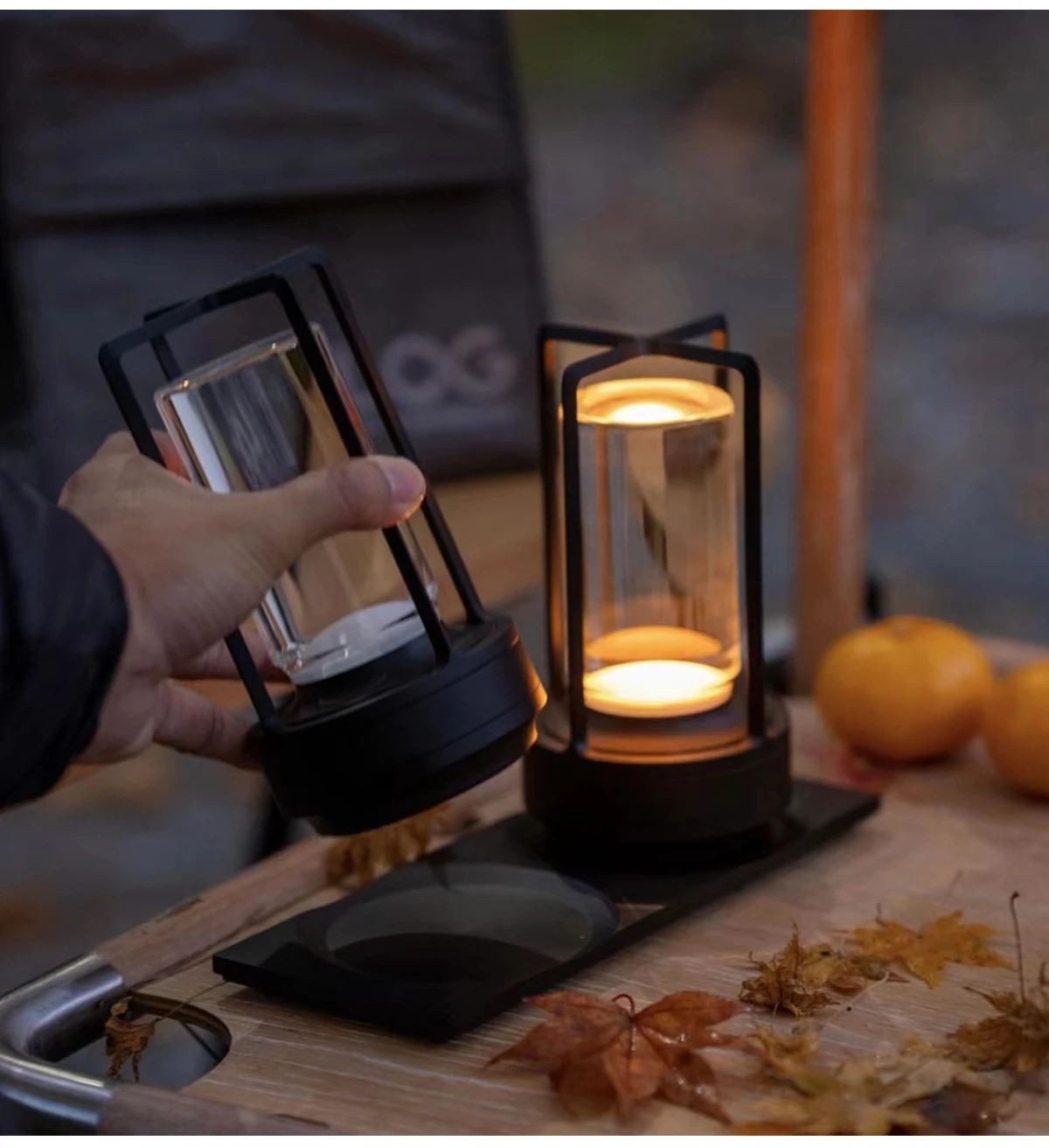Hand hält Lampe, daneben brennende Laterne, Orangen und Blätter.