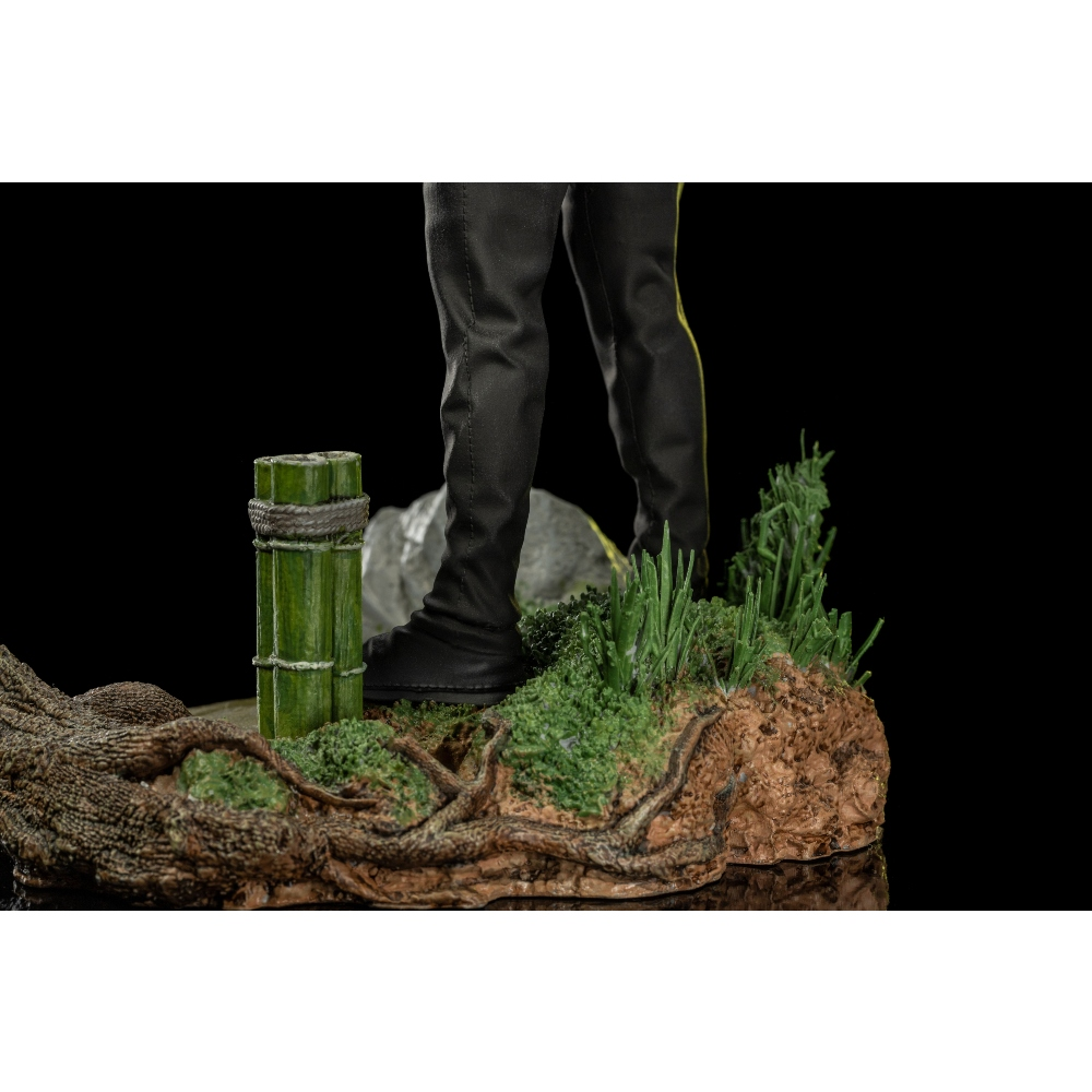 Eine Figur mit schwarzen Hosen steht auf einer felsigen Basis mit Bambus und Gras.