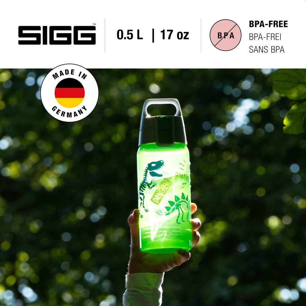 Grüne SIGG-Trinkflasche mit Dinosauriern, gehalten von einer Hand vor Bäumen.