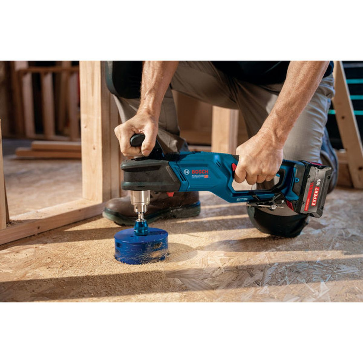 Una persona usa un trapano Bosch blu per tagliare un foro in una superficie di legno.